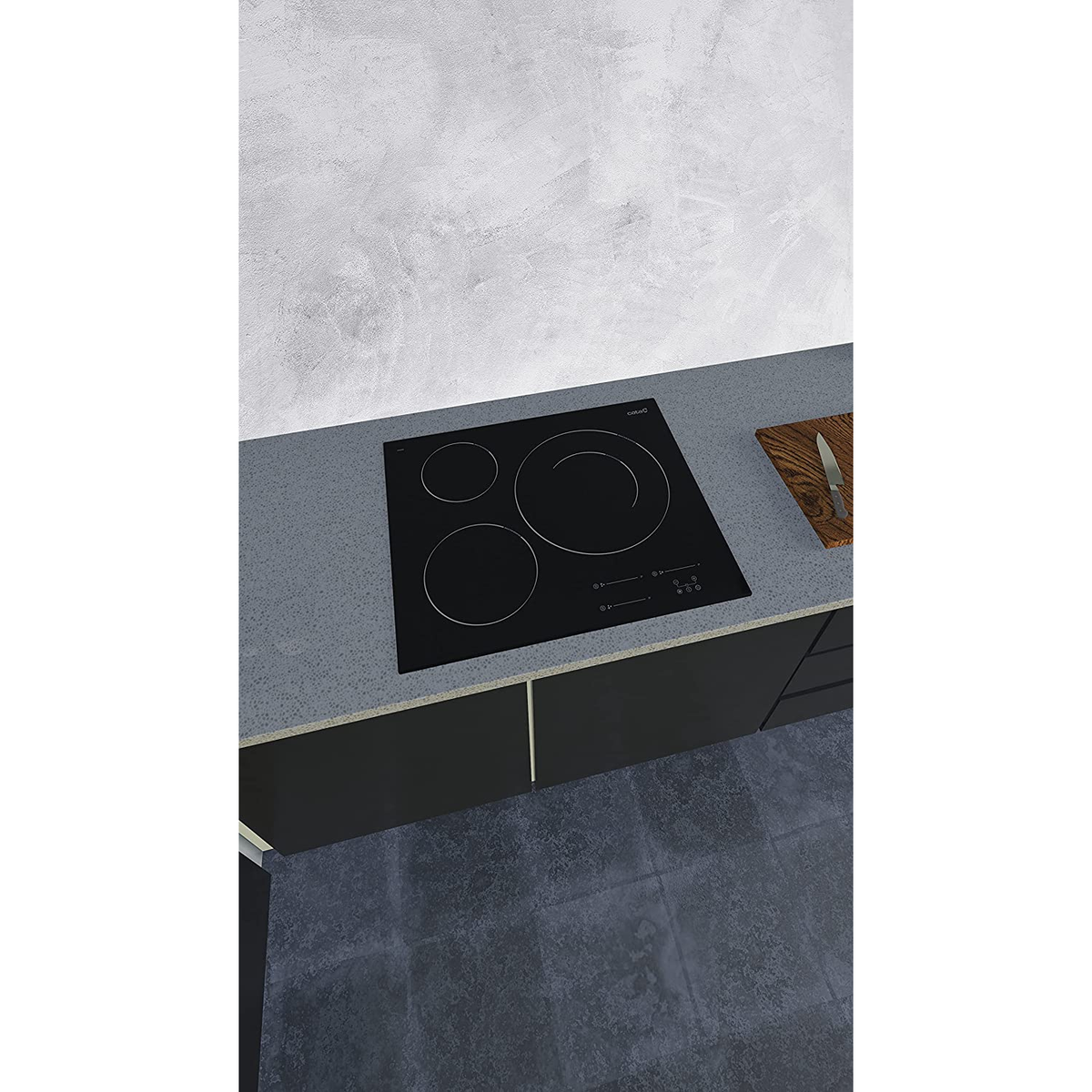 Placa de inducción en encimera con tabla de cortar y cuchillo en cocina.