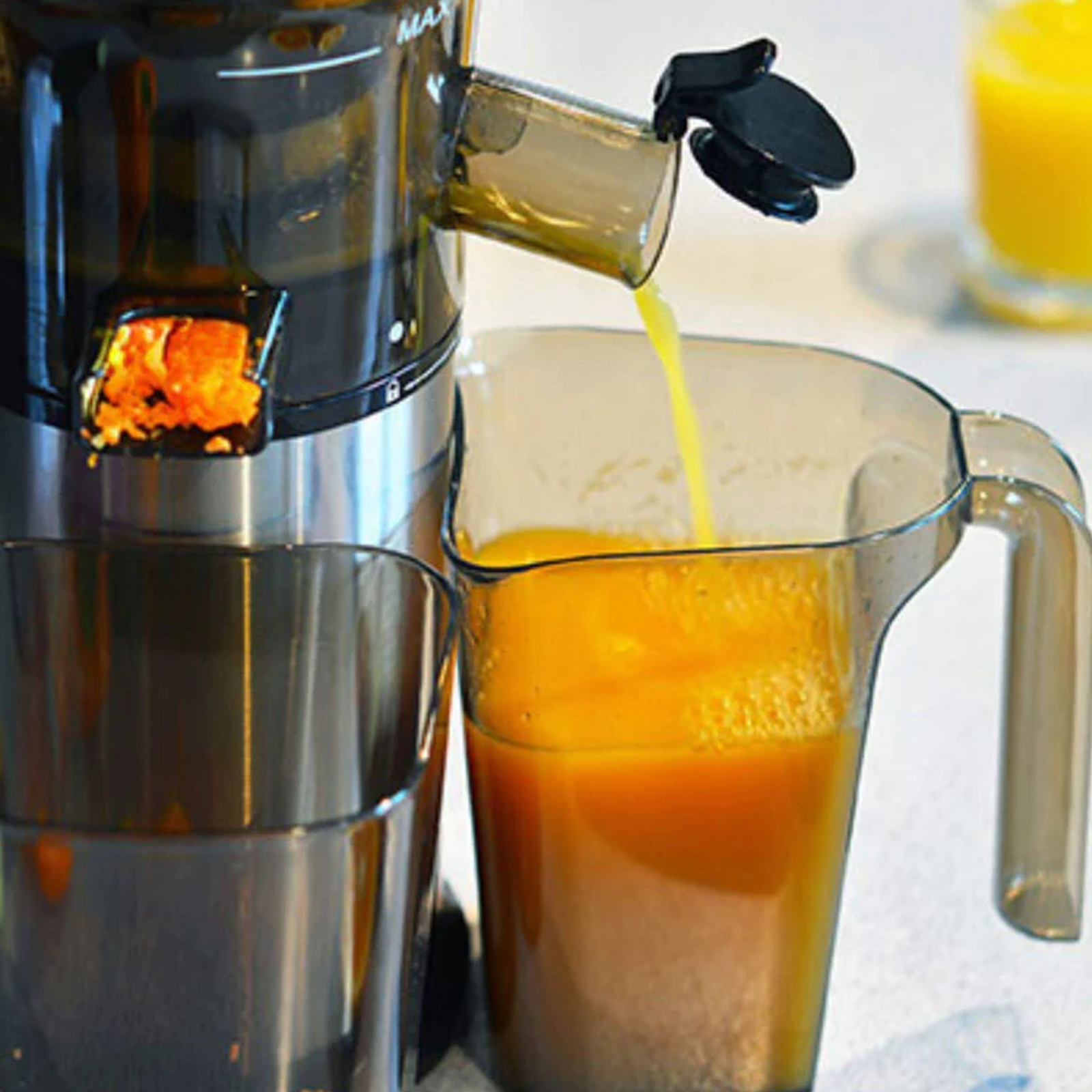Saft, der aus einem Entsafter in einen mit Orangensaft gefüllten Glaskrug gegossen wird.