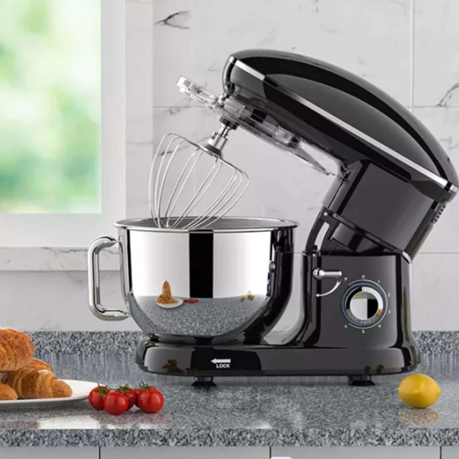 Schwarzer Küchenmixer mit Edelstahl-Schüssel. Croissants und Tomaten auf der Theke.