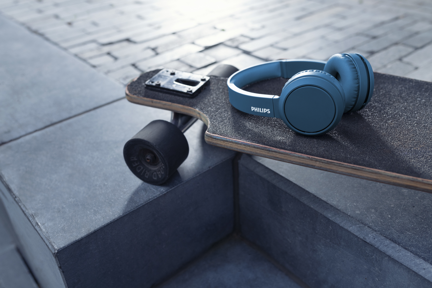Auriculares azules en una patineta. La patineta está sobre una superficie texturizada.