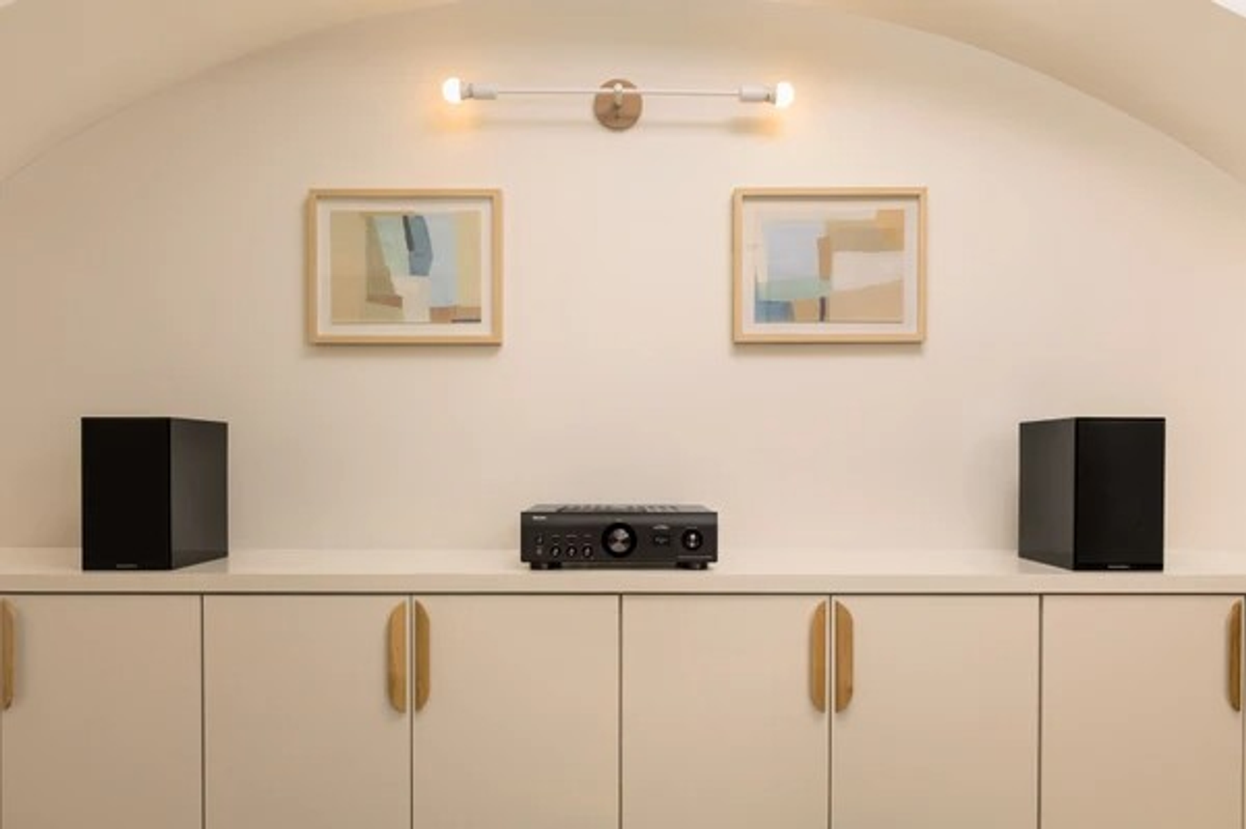 Raumeinrichtung mit weißem Schrank, zwei Lautsprechern, einem Receiver, zwei gerahmten Bildern und Lichtern.