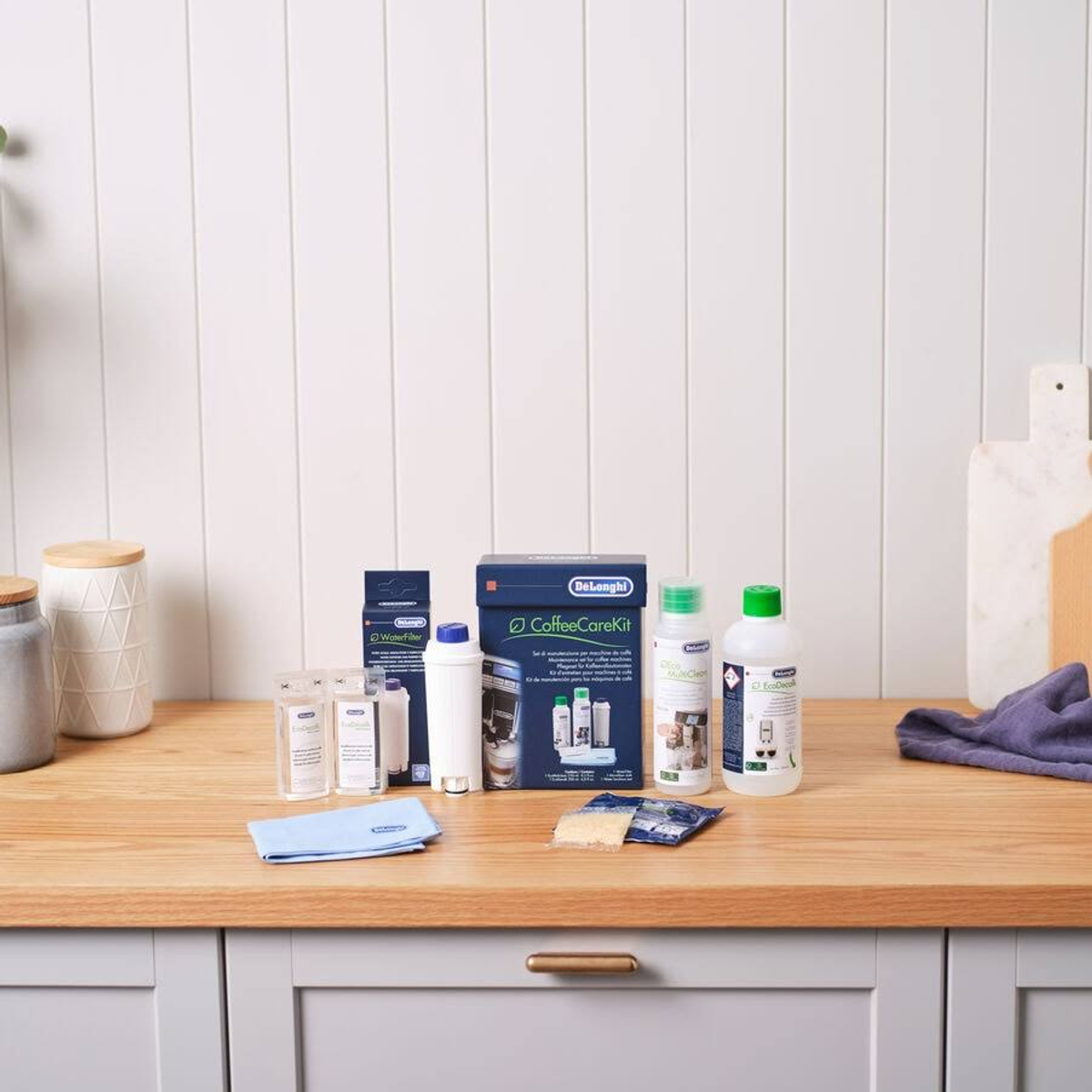 Kit de cuidado de cafetera con botellas, filtros y un paño de limpieza en una encimera.