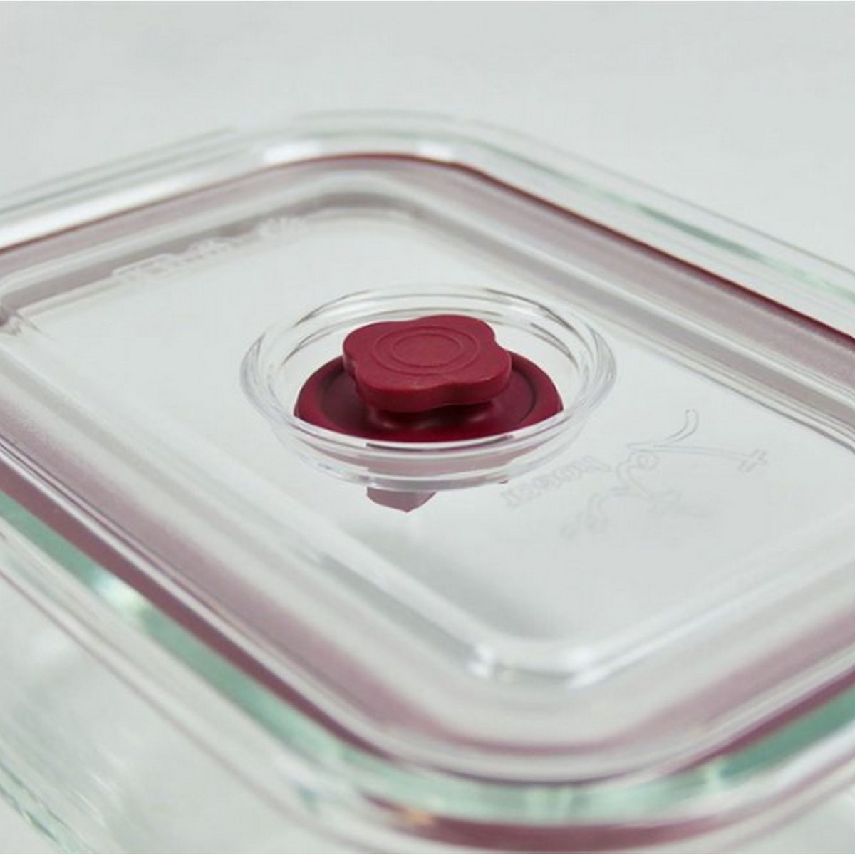 Tapa de recipiente de vidrio transparente con una ventilación roja en forma de flor.