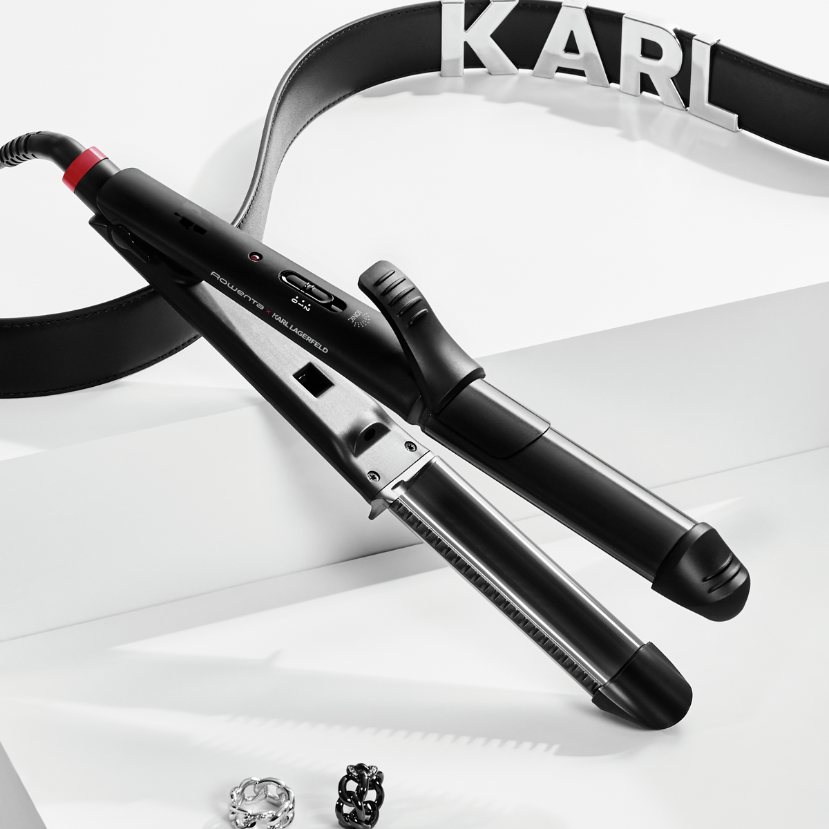 Zwei schwarze Haarstyling-Tools mit einem schwarzen Gürtel mit der Aufschrift KARL und Schmuck.