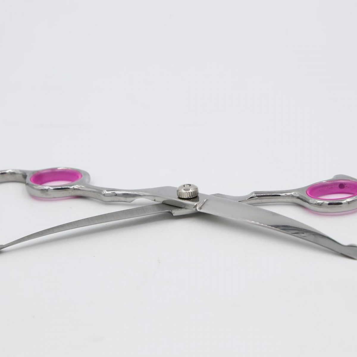 A pair of silver scissors with pink handles, lying on white surface.
