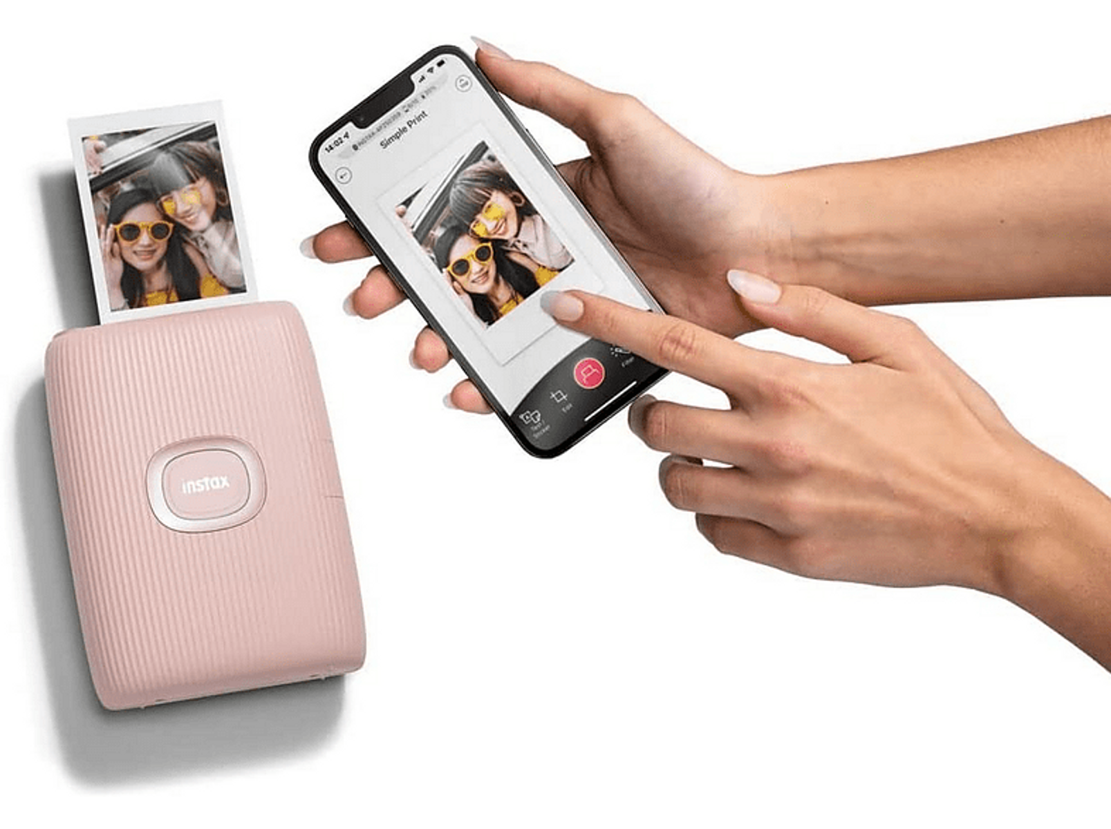 Różowa drukarka Instax obok smartfona pokazującego zdjęcie. Dłonie kobiety trzymające telefon.