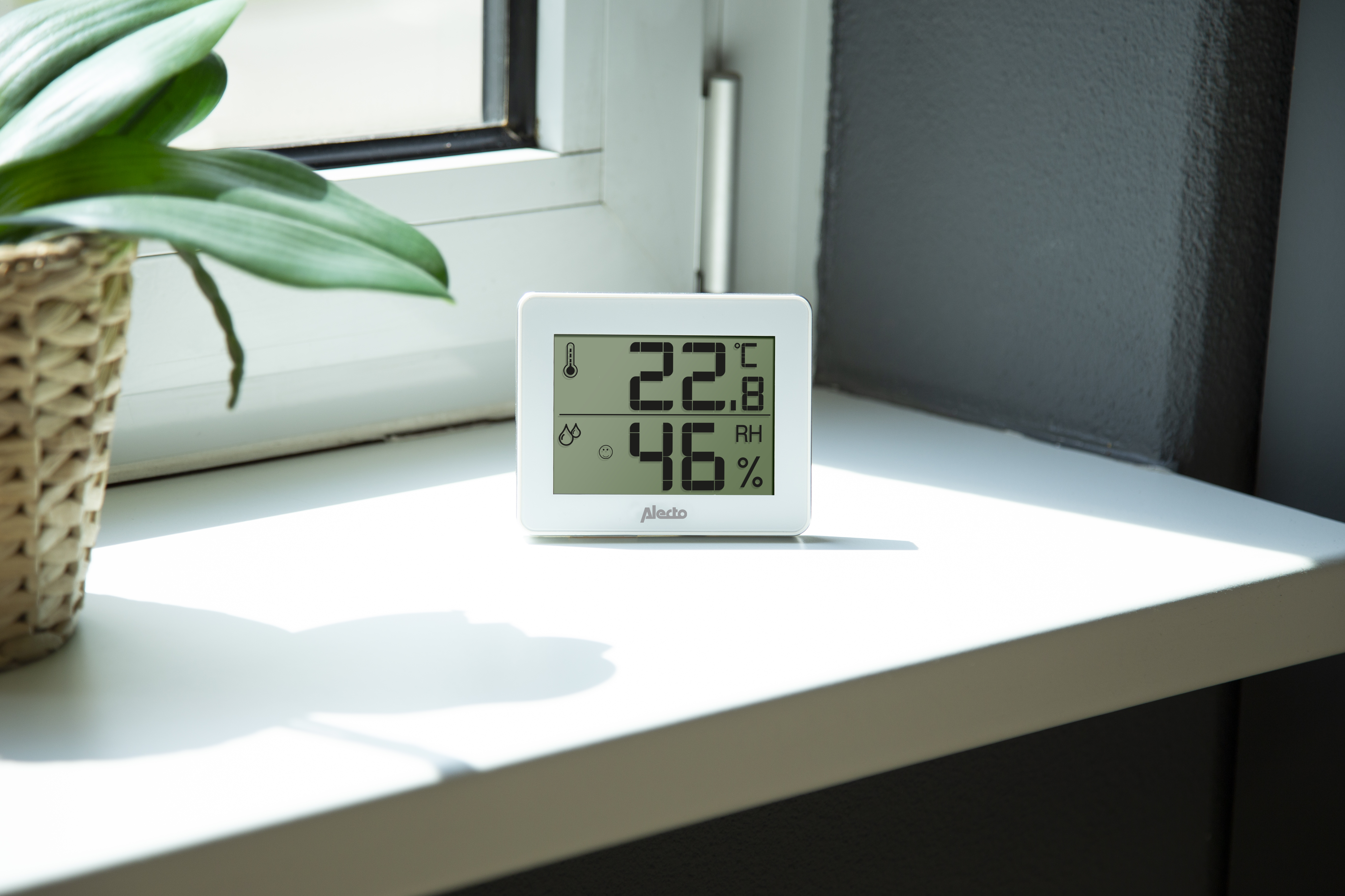 Ein digitales Thermometer, das Temperatur und Luftfeuchtigkeit auf einer weißen Fensterbank anzeigt.