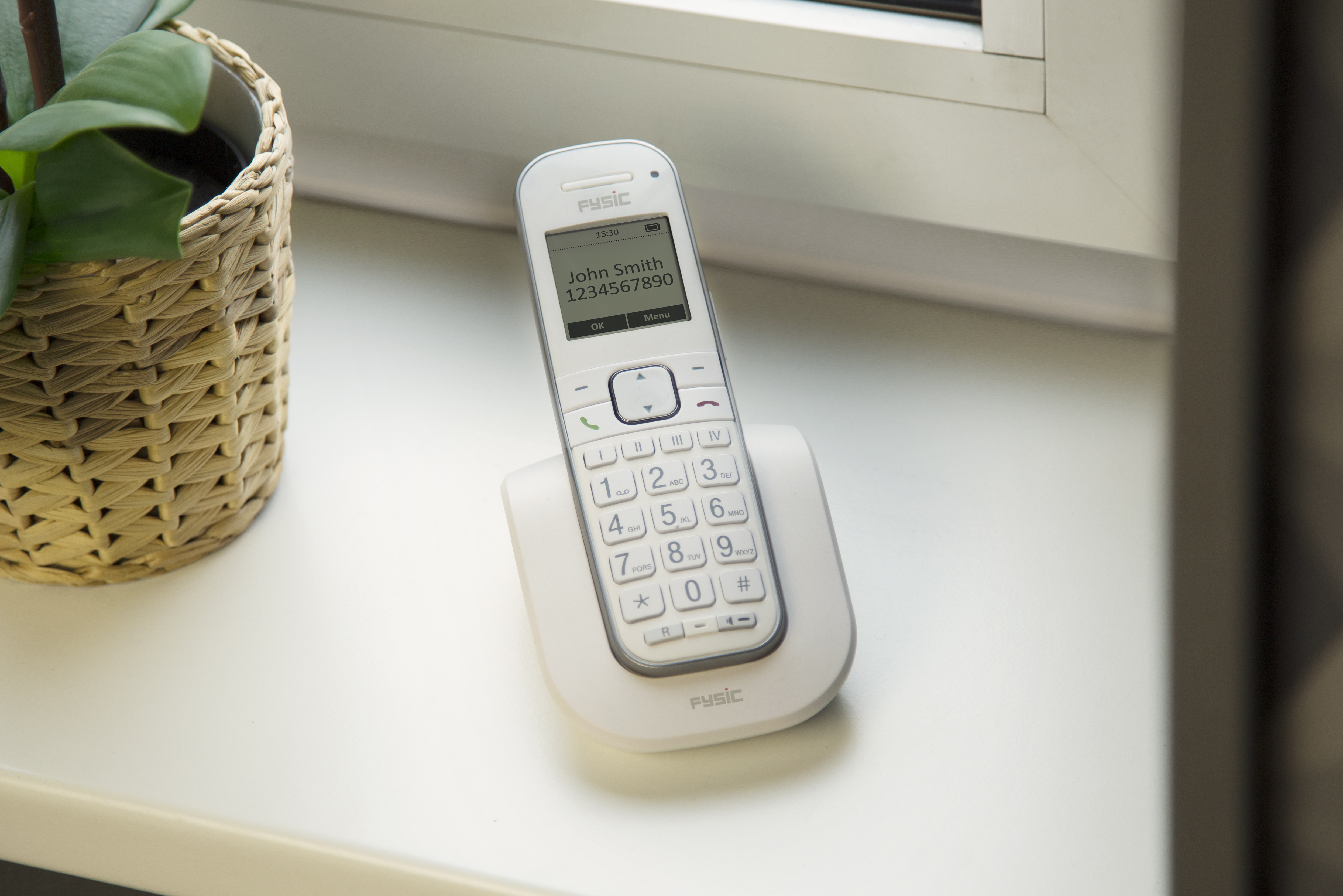Ein weißes schnurloses Telefon mit Bildschirm, der einen Kontakt anzeigt, auf weißer Basis.