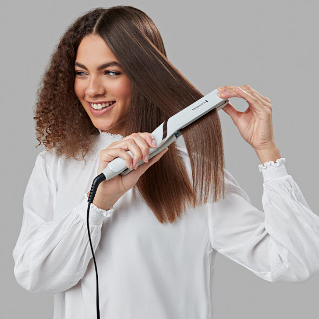 Una donna con i capelli ricci si sta lisciando i capelli con una piastra bianca.