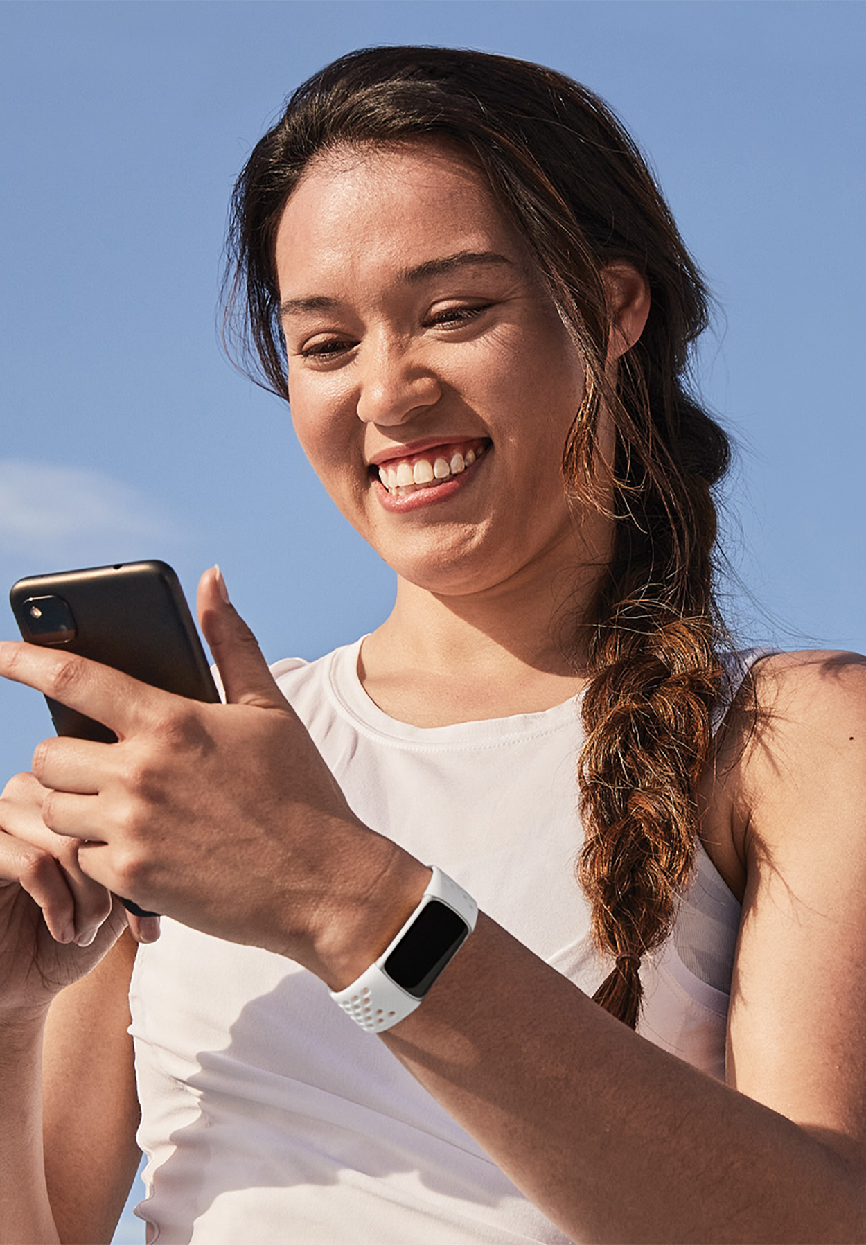 Eine Frau hält ein Telefon und trägt einen Fitness-Tracker vor blauem Himmel.