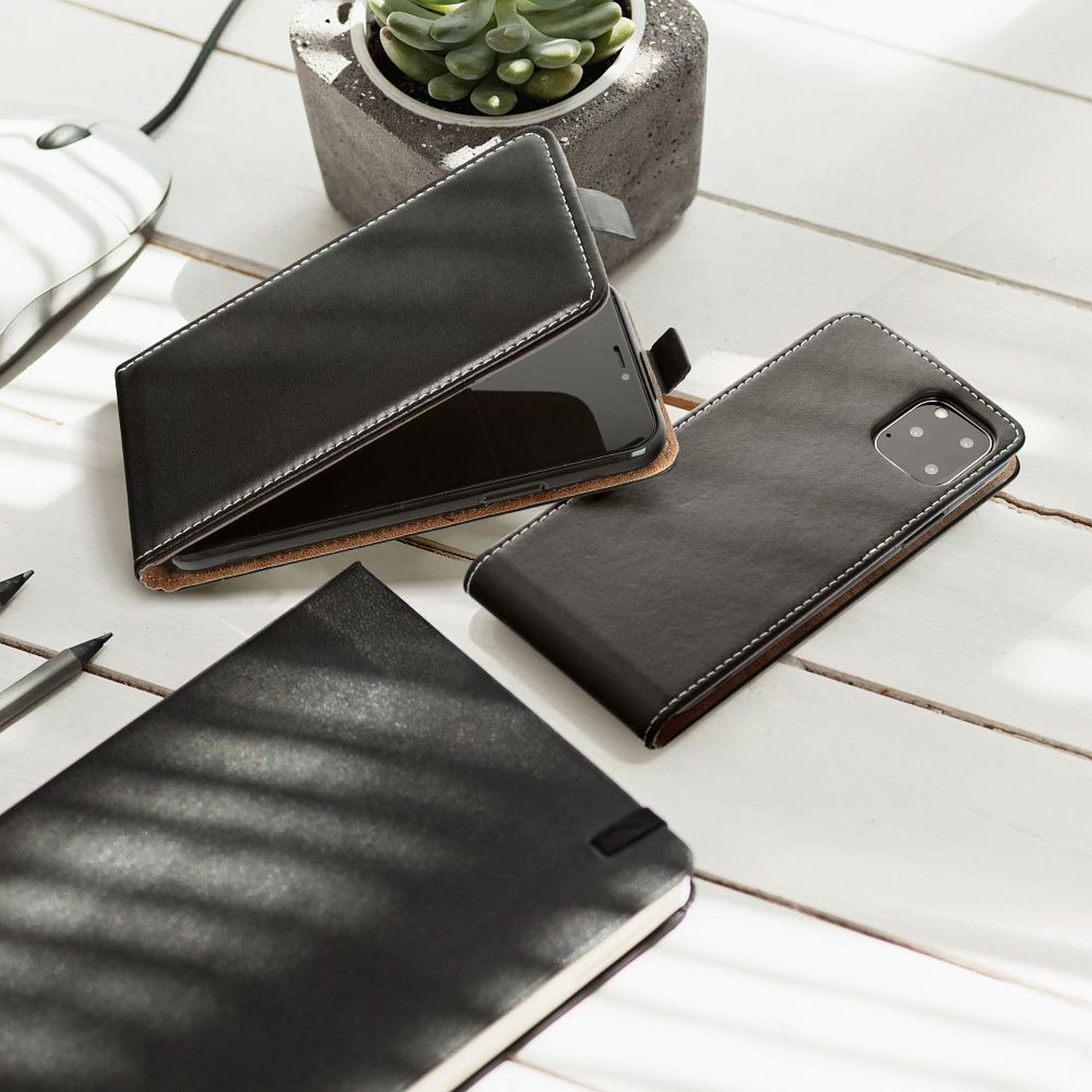 Schwarze Handyhüllen mit Telefon, Notizbuch und Stift auf weißem Holzschreibtisch.
