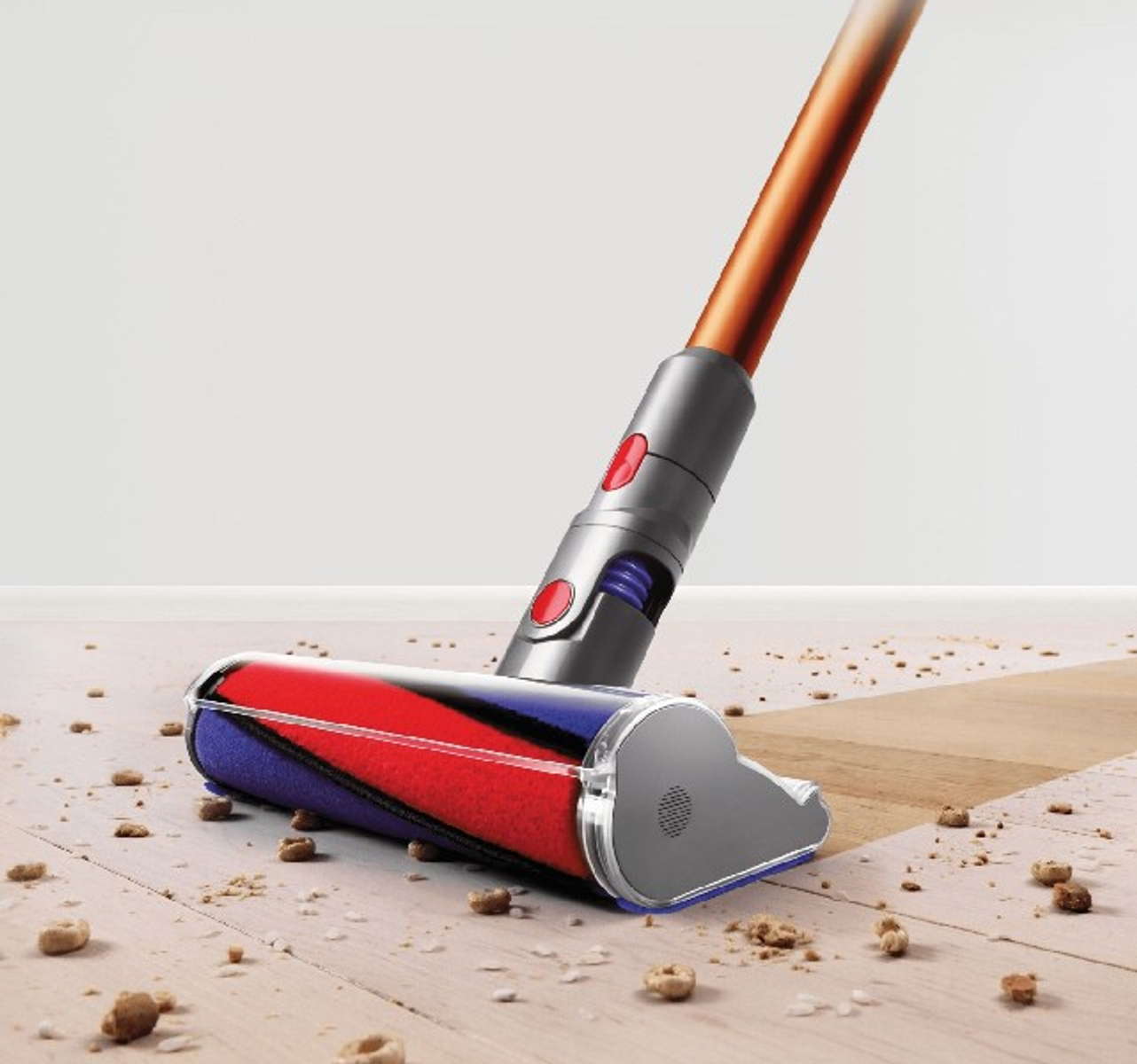 Dyson Staubsaugerkopf auf einem Holzboden. Auf dem Boden sind Rückstände verstreut. Der Griff ist sichtbar.