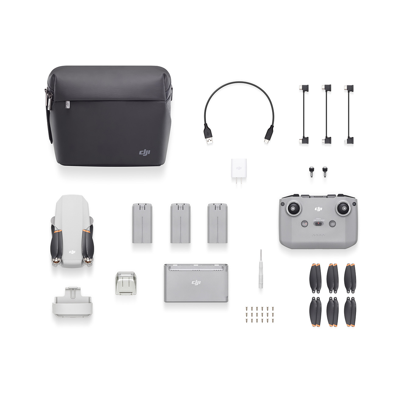 Ein Drohnen-Kit mit grauem Koffer, Drohne, Zubehör, Ladegerät und Batterien auf weißem Untergrund.