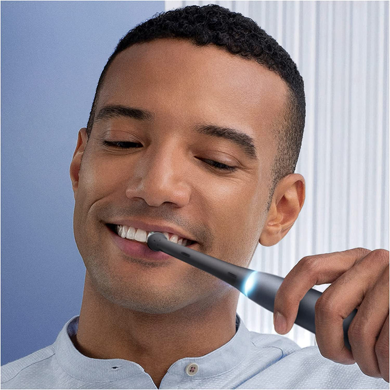 Un uomo si lava i denti con uno spazzolino elettrico nero. Sorride, lo spazzolino è illuminato di blu.