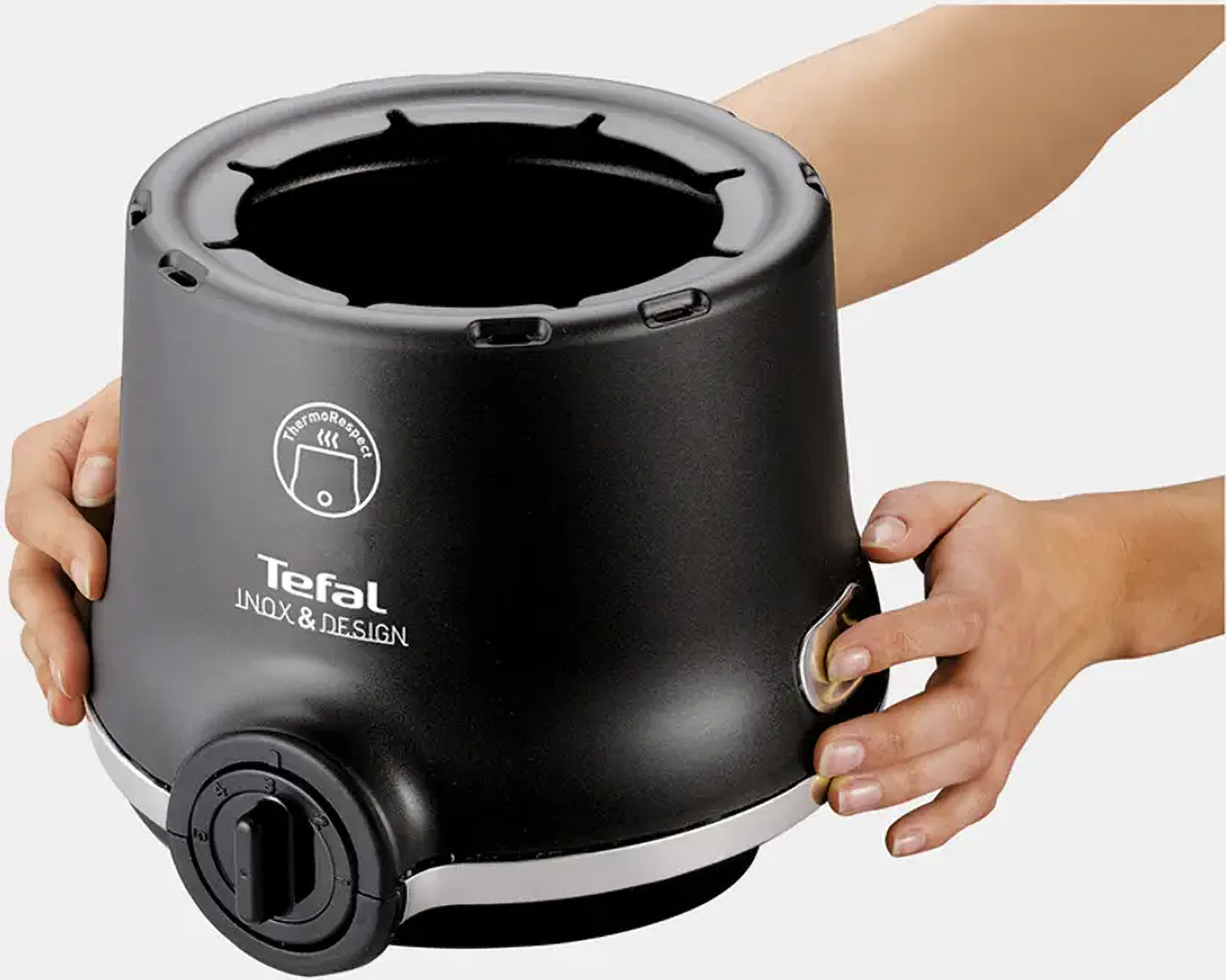 Czarna podstawa urządzenia Tefal z trzymającymi ją dłońmi. Obecne jest pokrętło i białe akcenty.