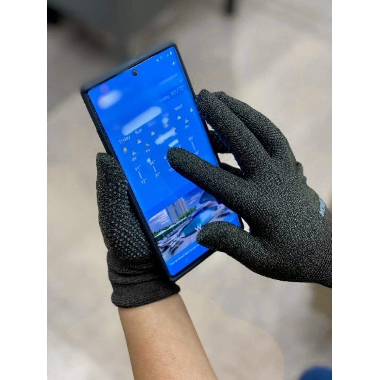 Eine Person, die schwarze Handschuhe trägt, benutzt ein Telefon und zeigt eine Wetter-App auf dem Bildschirm.