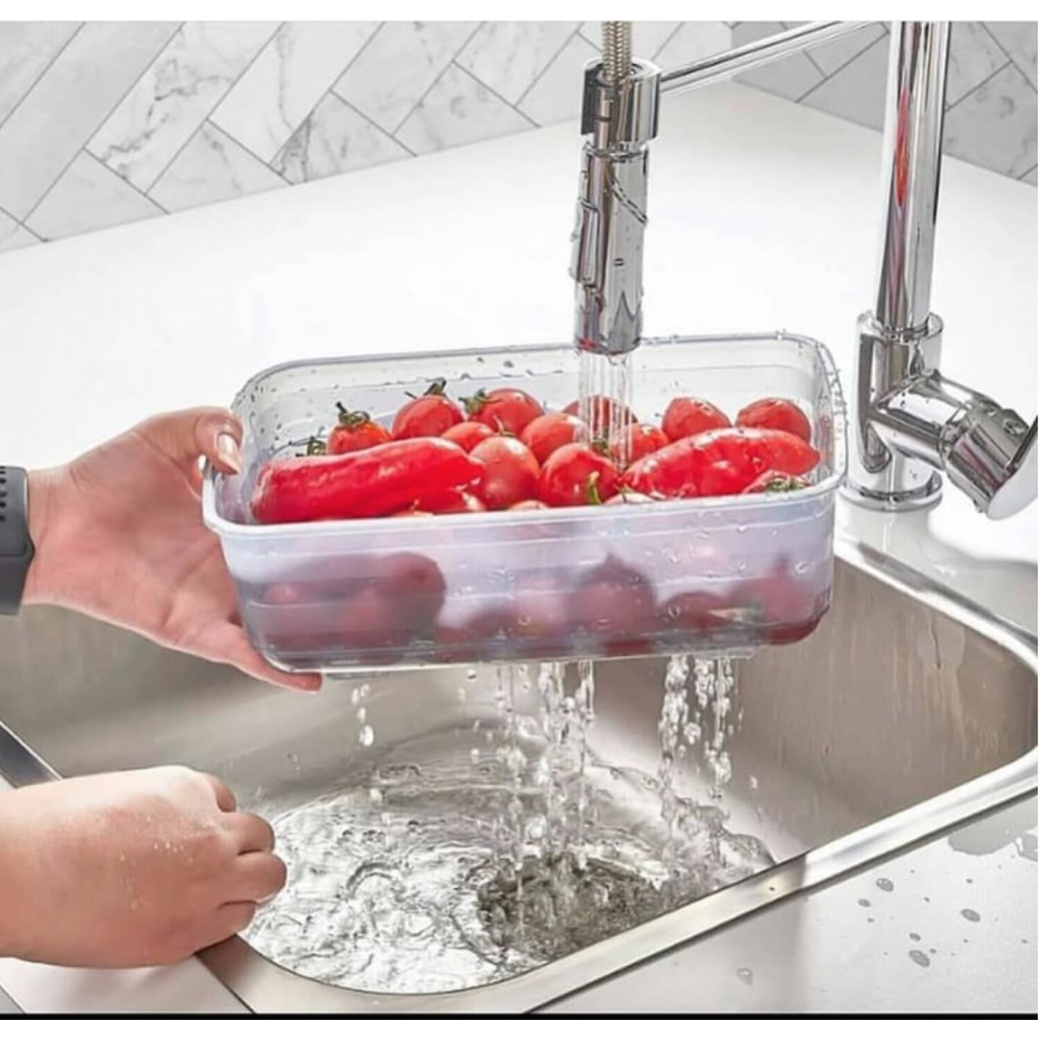 Ein Behälter mit Tomaten wird unter einem Wasserhahn in einem Edelstahlbecken gewaschen.