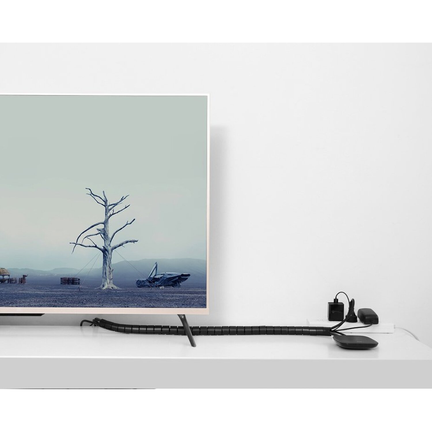 TV con scena di albero su un tavolo bianco. Organizzatore per cavi nero e dispositivi neri.