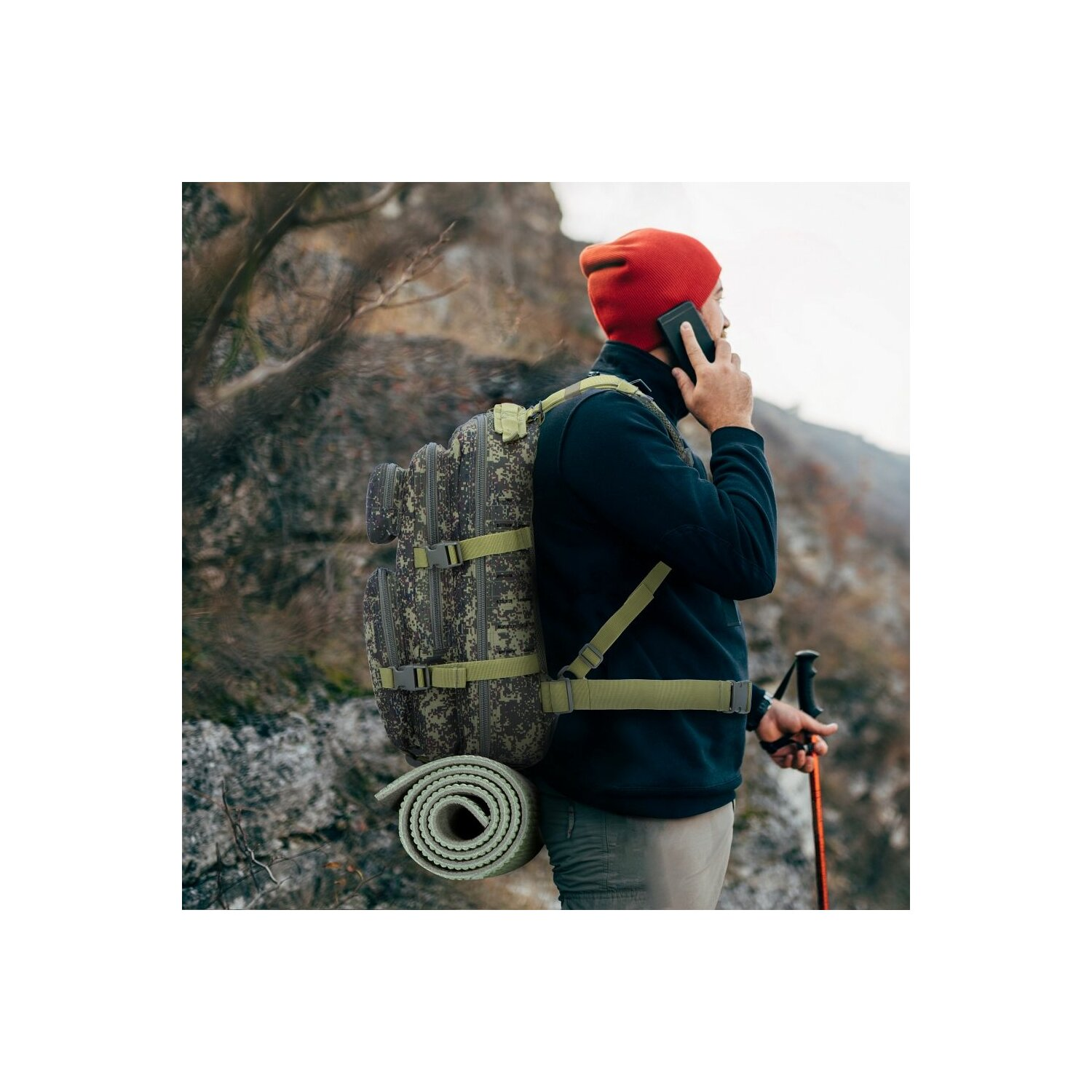 Mann mit Rucksack und roter Mütze, telefoniert. Wandern in der Natur, trägt eine Matte.