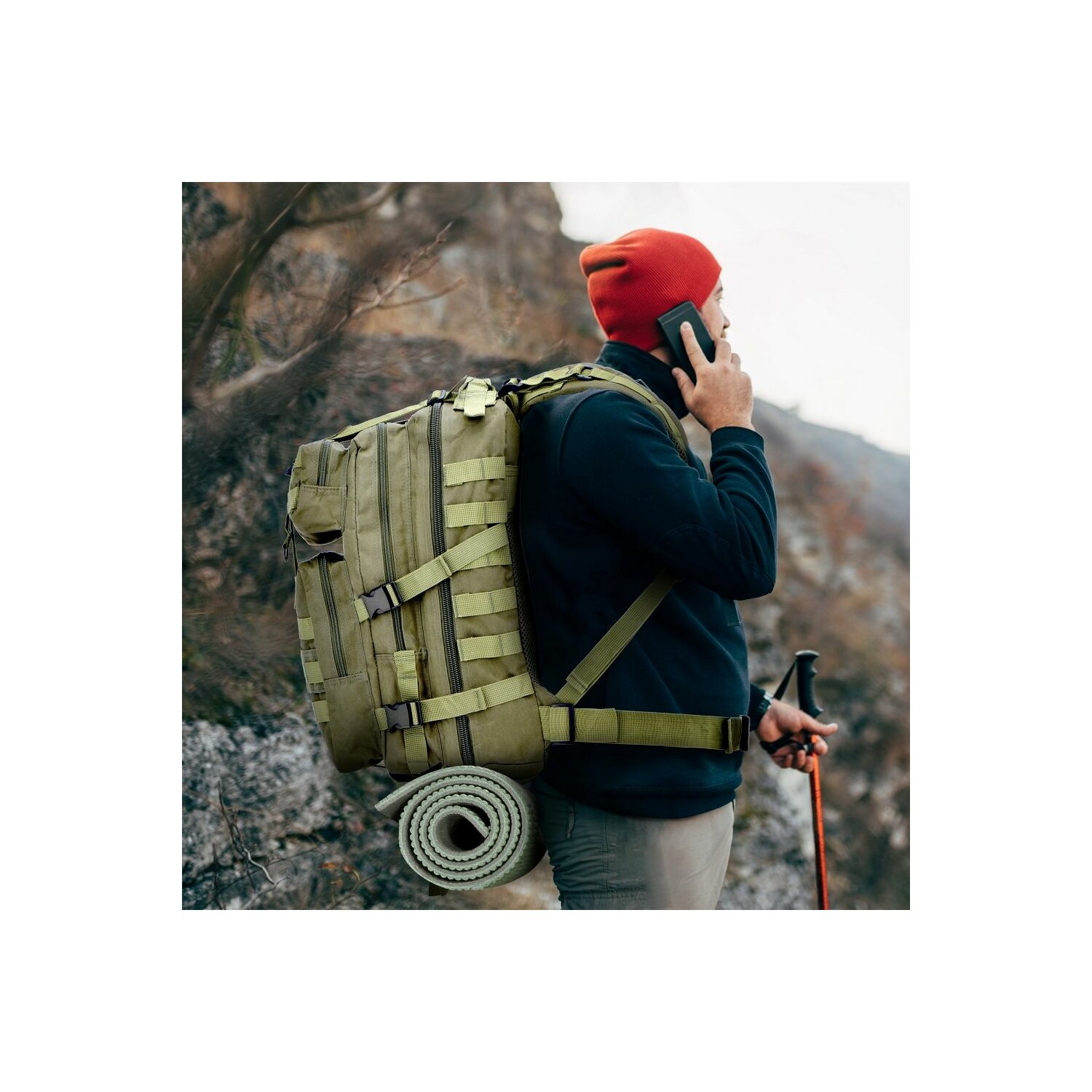 Ein Mann mit roter Mütze und Rucksack auf felsigem Hügel, telefoniert.