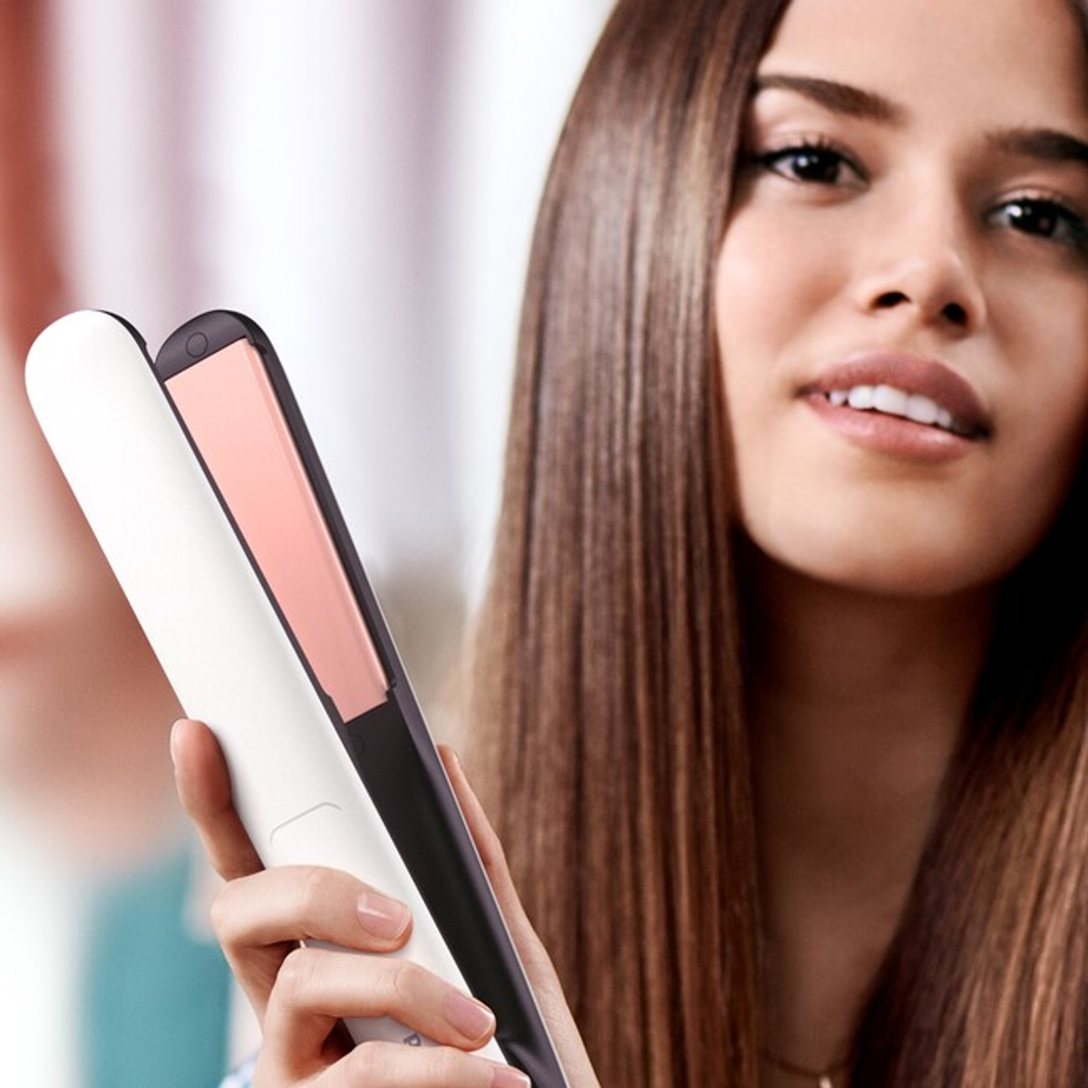 Una donna che tiene una piastra per capelli bianca con piastre rosa, sorridendo alla fotocamera.