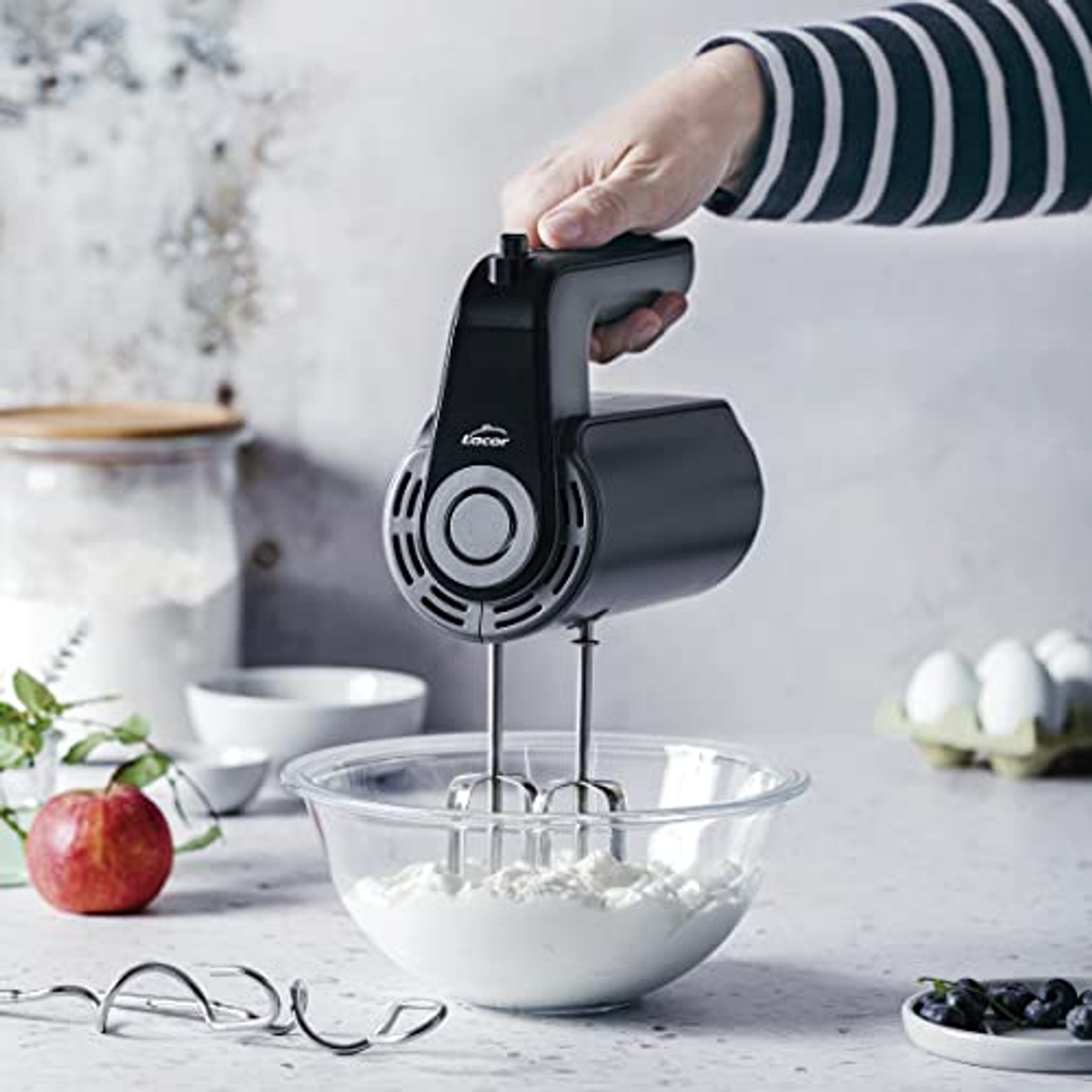 Eine Hand hält einen schwarzen Mixer, Zutaten in einer Schüssel.