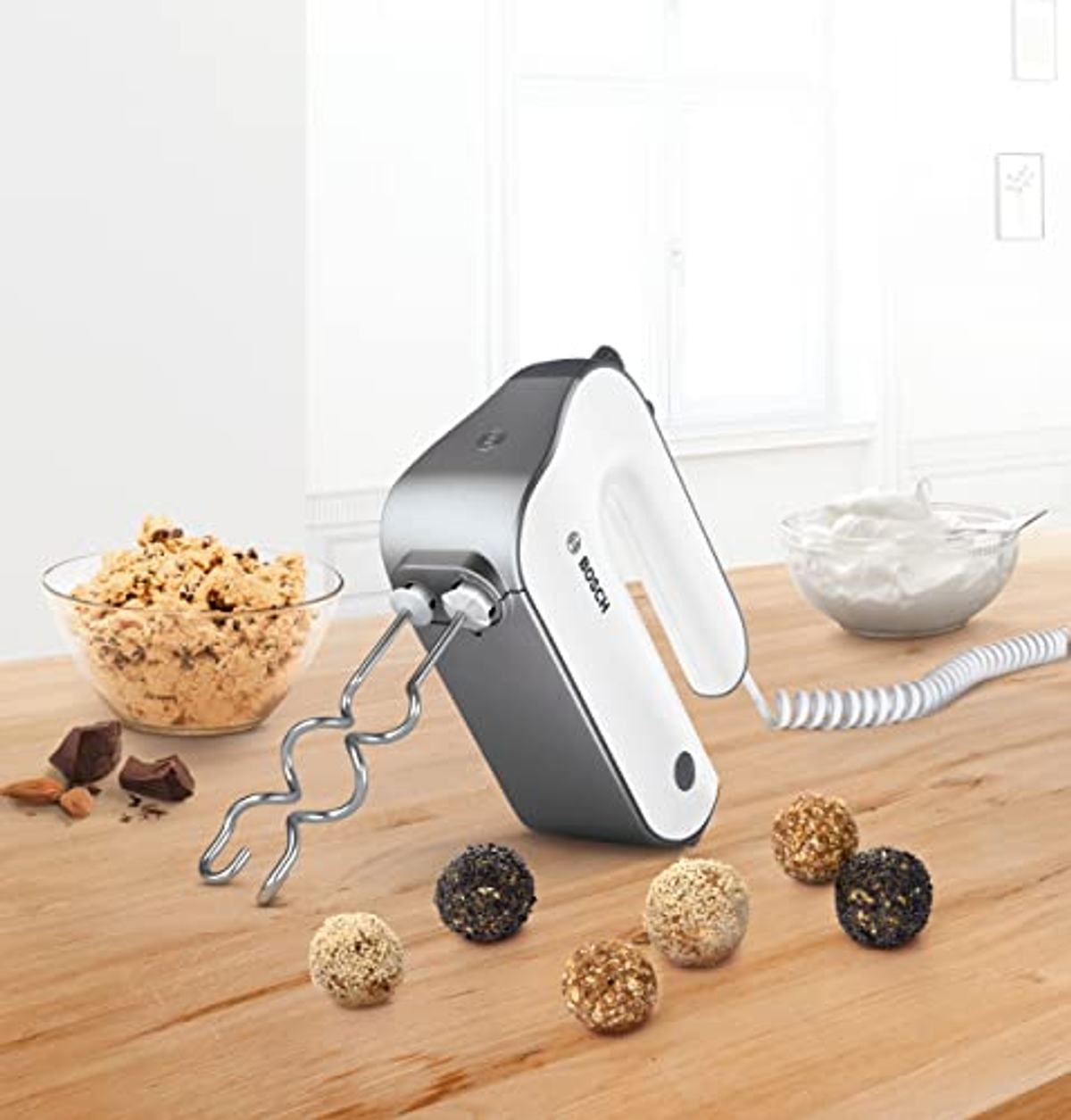 Batidora de mano con accesorios y alimentos en mesa de madera.