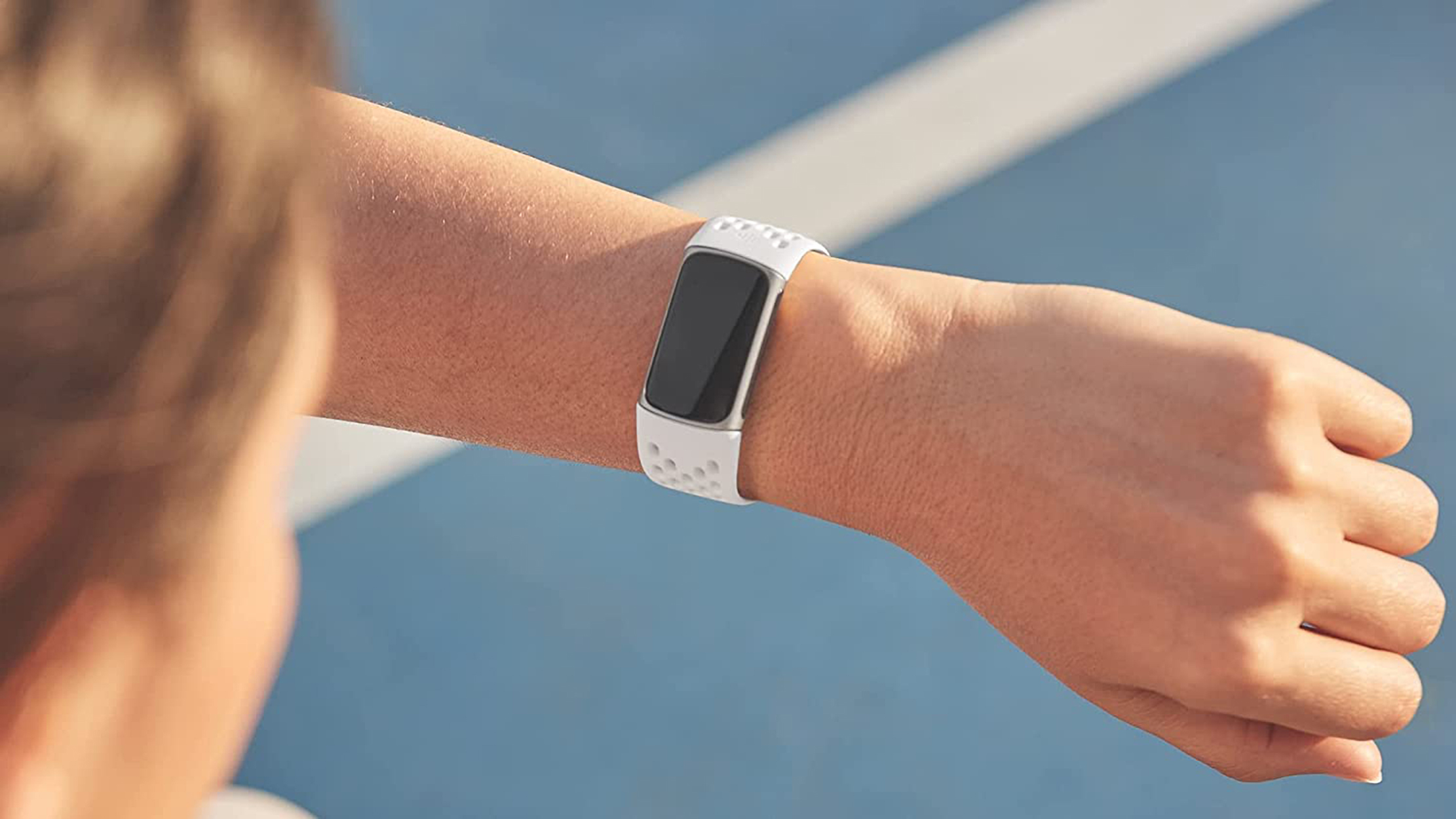 Eine Person trägt eine weiße Smartwatch mit schwarzem Bildschirm. Der Arm ist ausgestreckt, der Hintergrund ist unscharf.