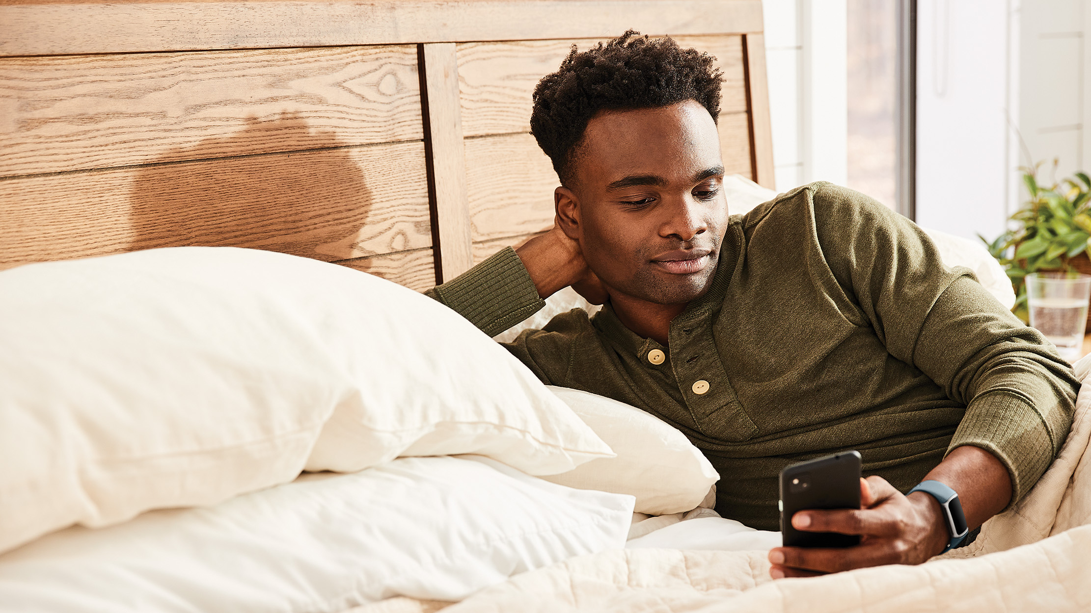 Ein Mann im Bett, der auf sein Handy schaut. Er stützt seinen Kopf auf seine Hand.