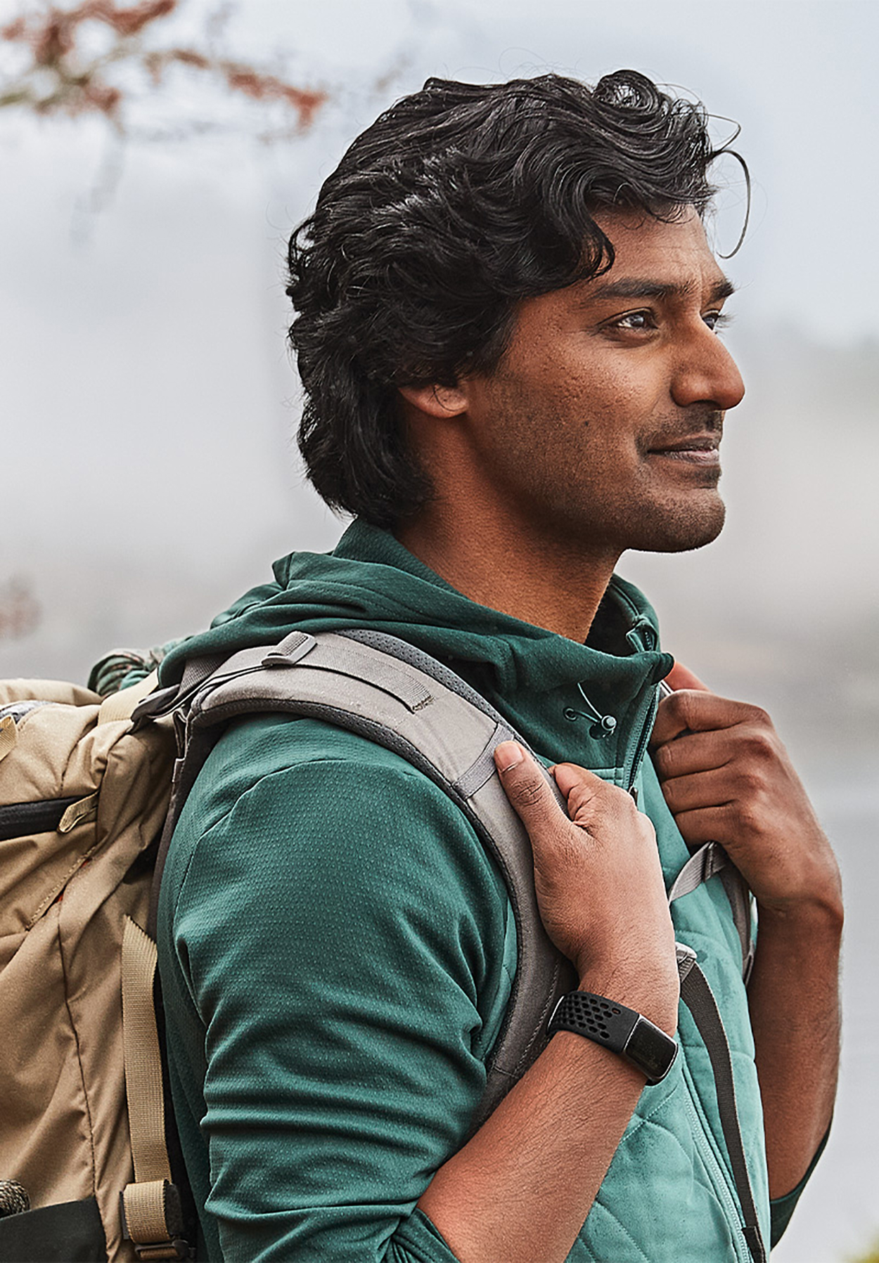 Mann in einer grünen Jacke mit einem Rucksack. Er schaut nach rechts. Outdoor- und neblige Umgebung.