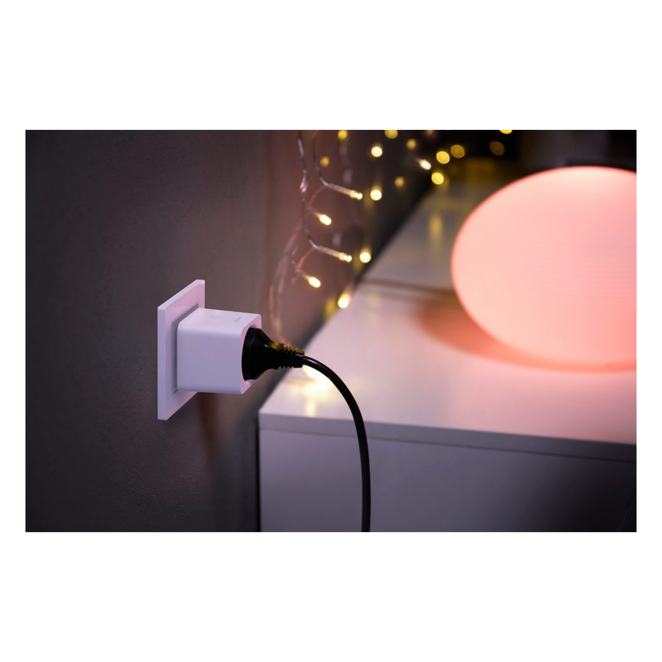 White smart plug plugged into a wall outlet, with a black cable and a pink light.