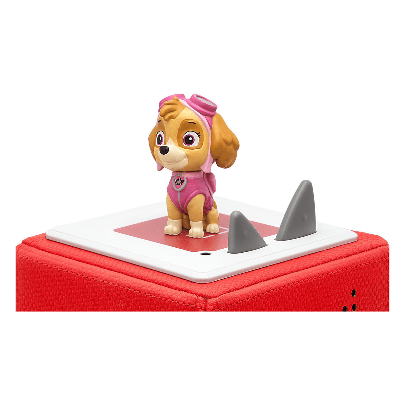 Skye-Spielzeugfigur von Paw Patrol auf einer roten Box. Zwei graue Haifischflossen stehen auf weißer Fläche.