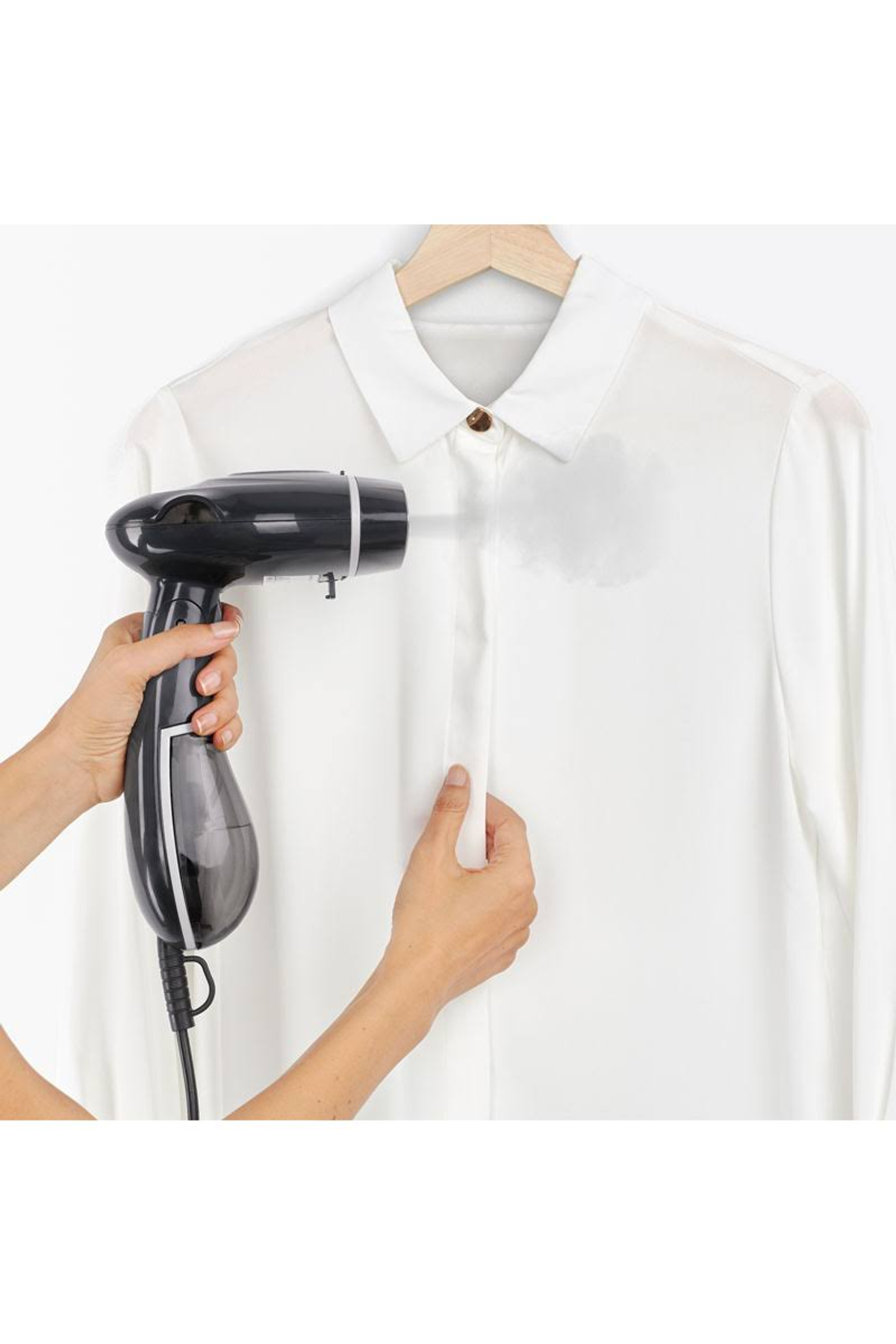Donna che stira una camicia bianca su un appendiabiti con un vaporizzatore nero. Sfondo bianco.