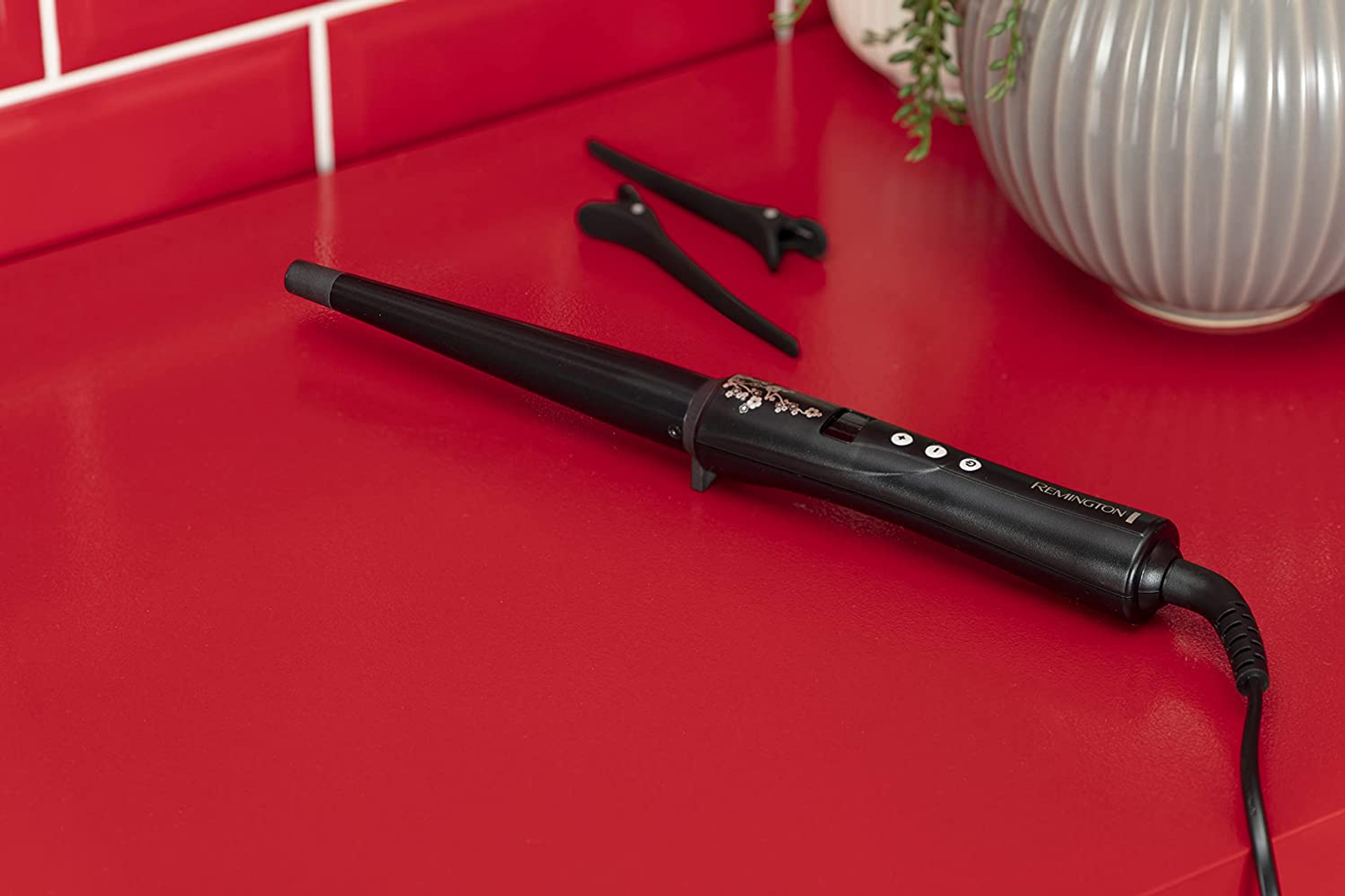 Arricciacapelli nero con accessori su una superficie rossa.