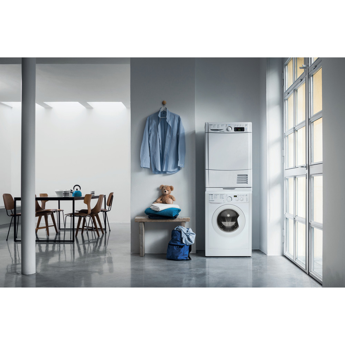 Toma interior de un espacio habitable moderno con lavadora, secadora y muebles. La habitación es luminosa.