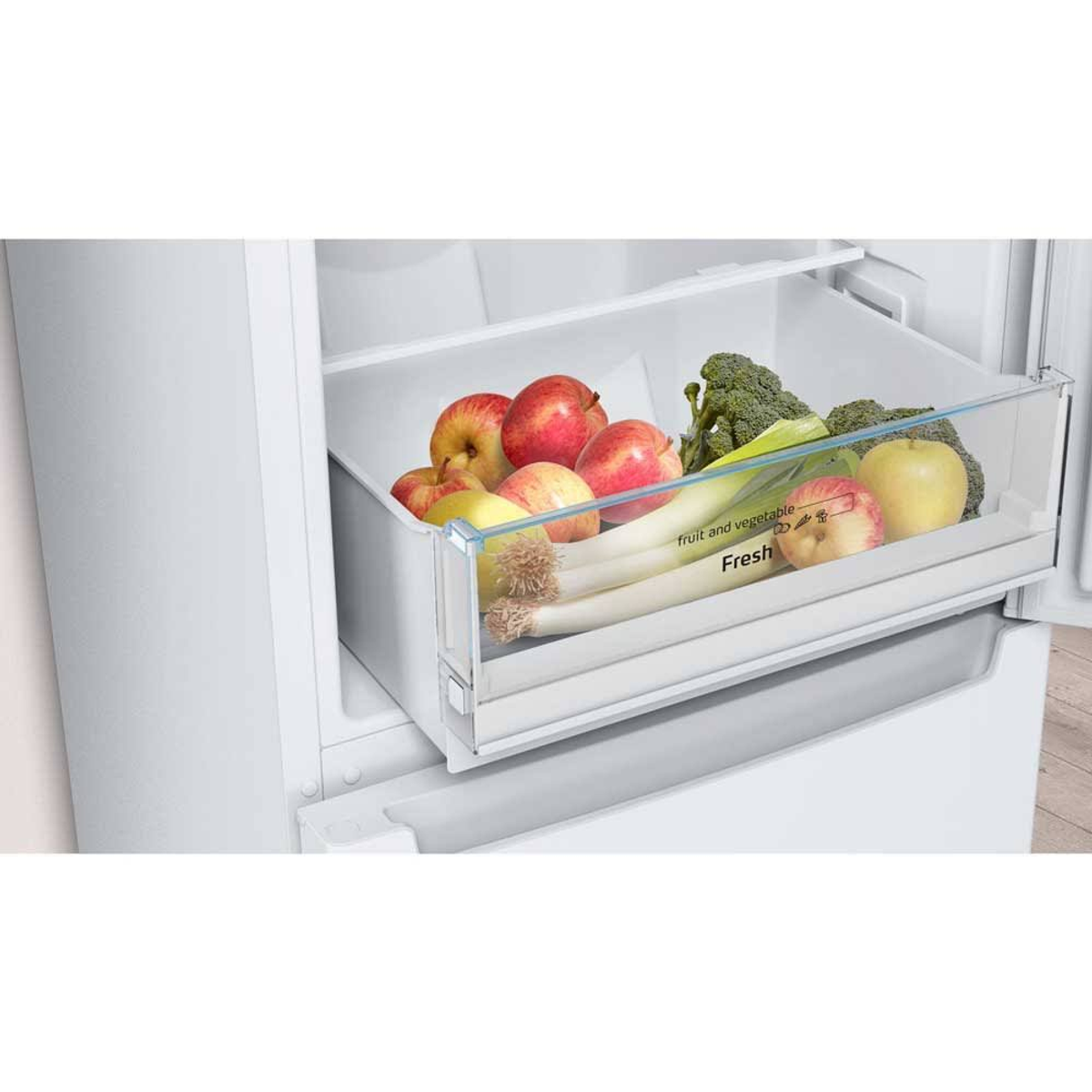 Cajón transparente en un refrigerador lleno de manzanas, brócoli y puerros.