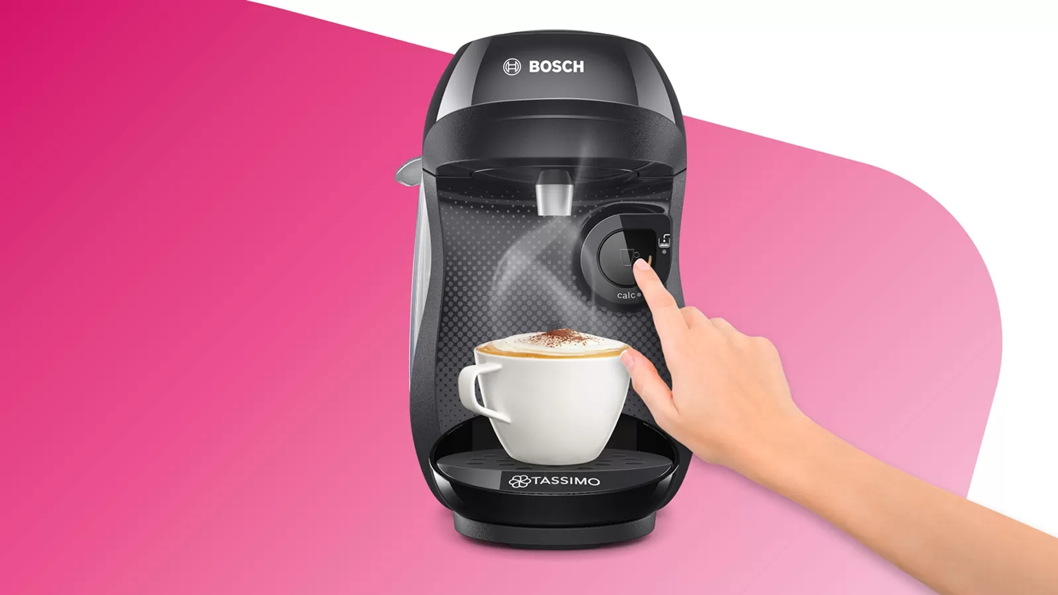 Una mano toca una cafetera Bosch Tassimo negra, con una taza de capuchino debajo del surtidor.