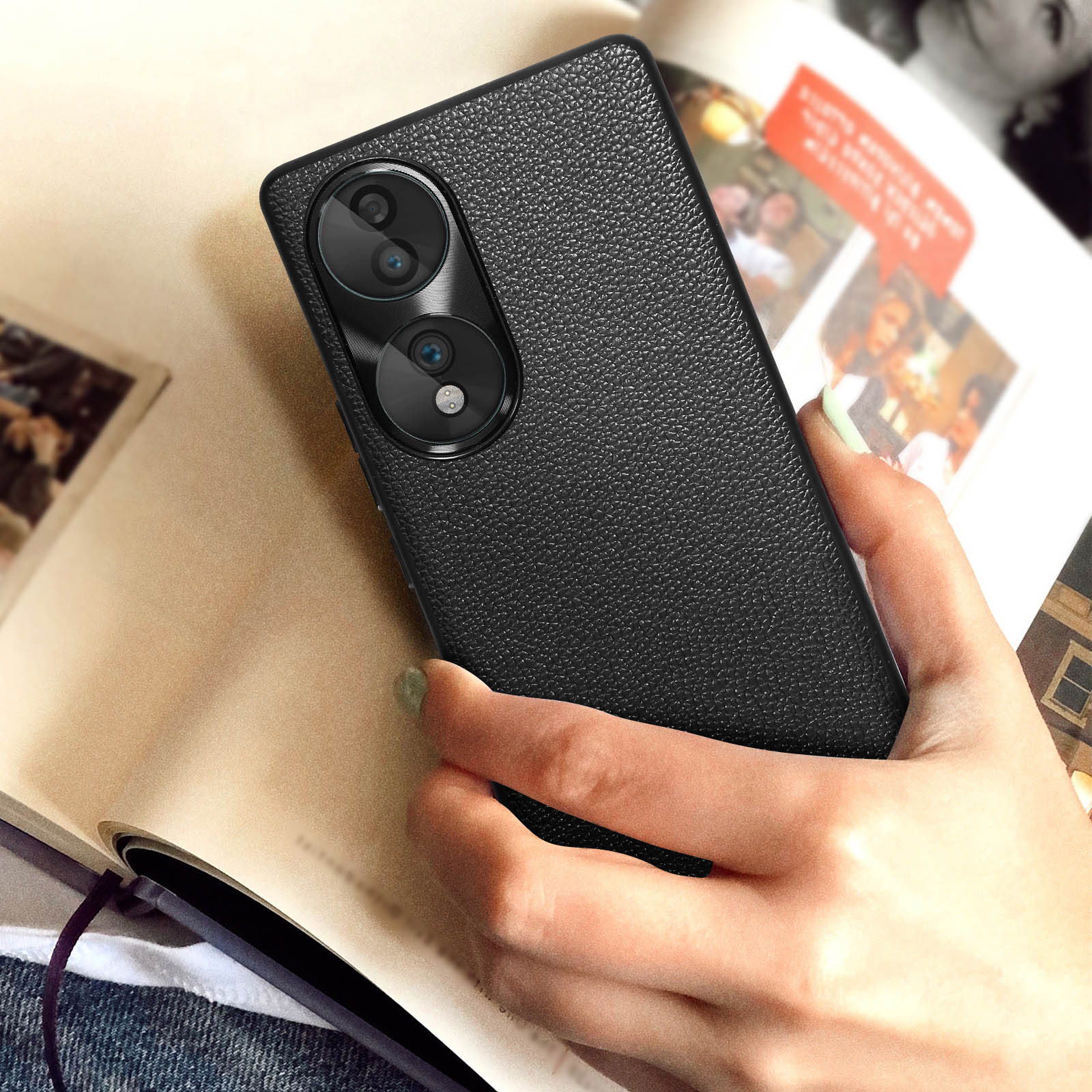 Custodia per telefono in pelle nera con fotocamera a doppia lente, tenuta in mano su libro aperto.