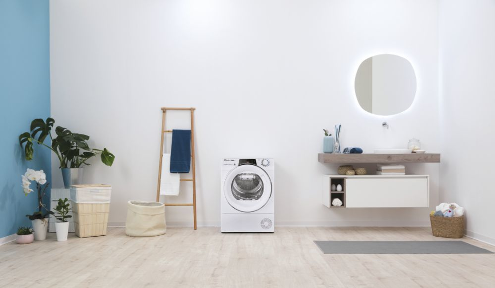 Escena de baño moderno. Incluye secadora, escalera de madera con toallas, plantas y espejo.