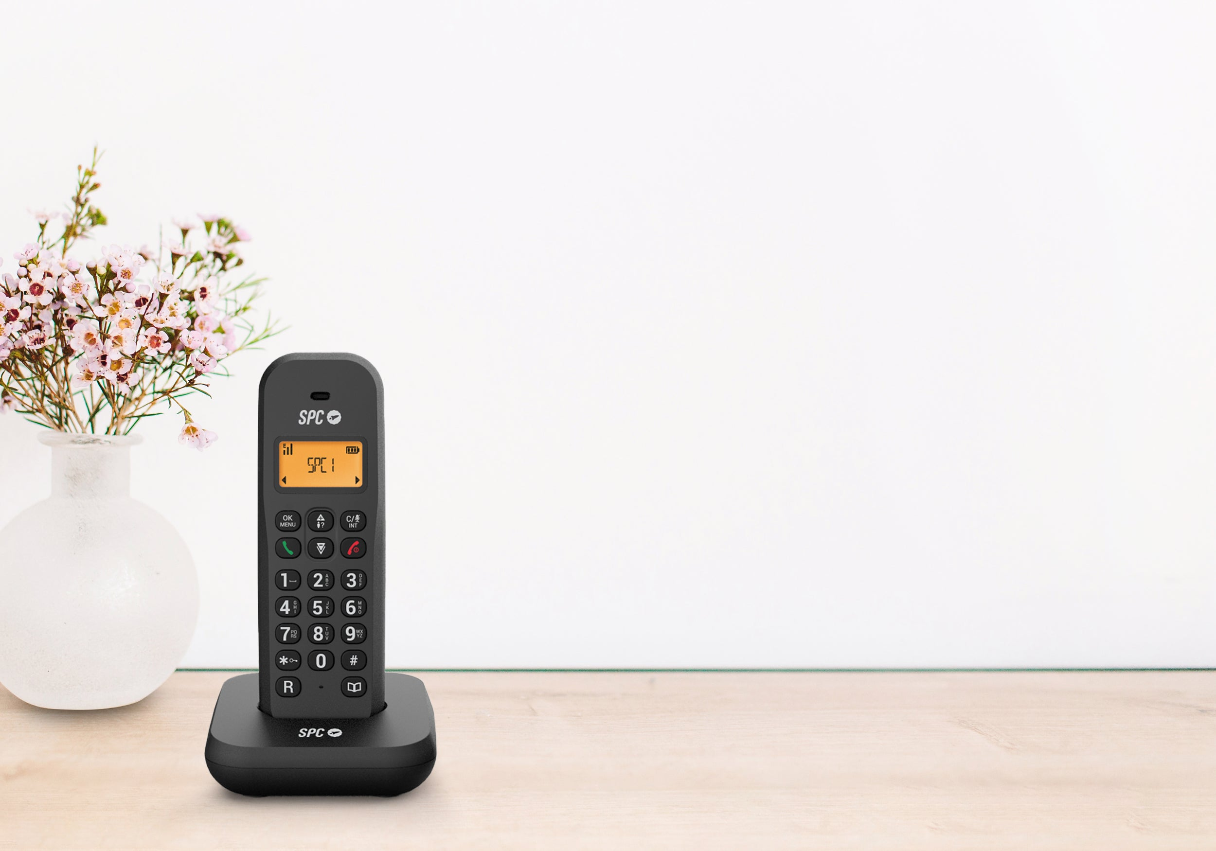 Telefono cordless nero su superficie in legno, vaso bianco e fiori.