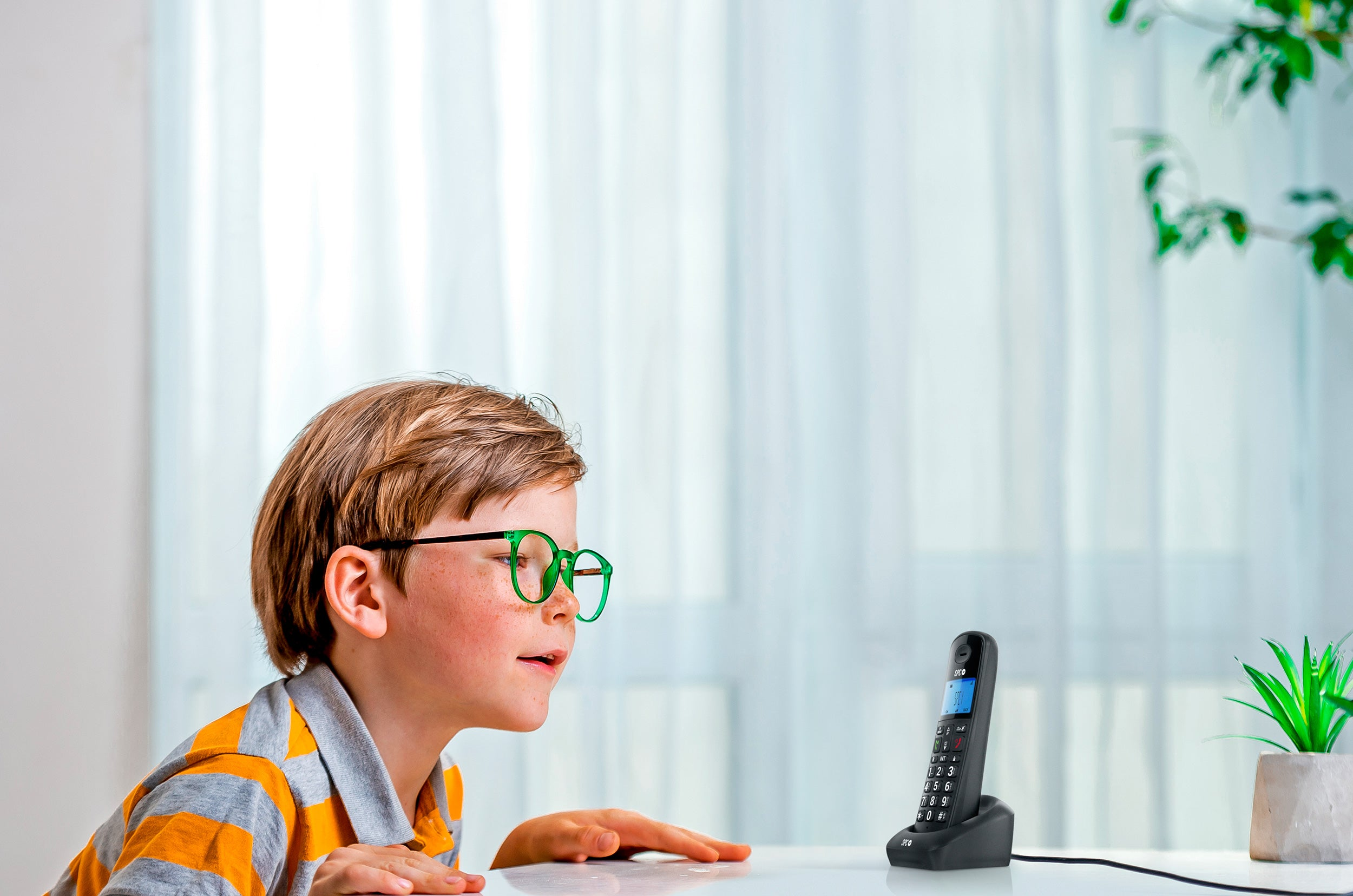 Ragazzo che parla al telefono cordless. Indossa occhiali e una maglia a righe.