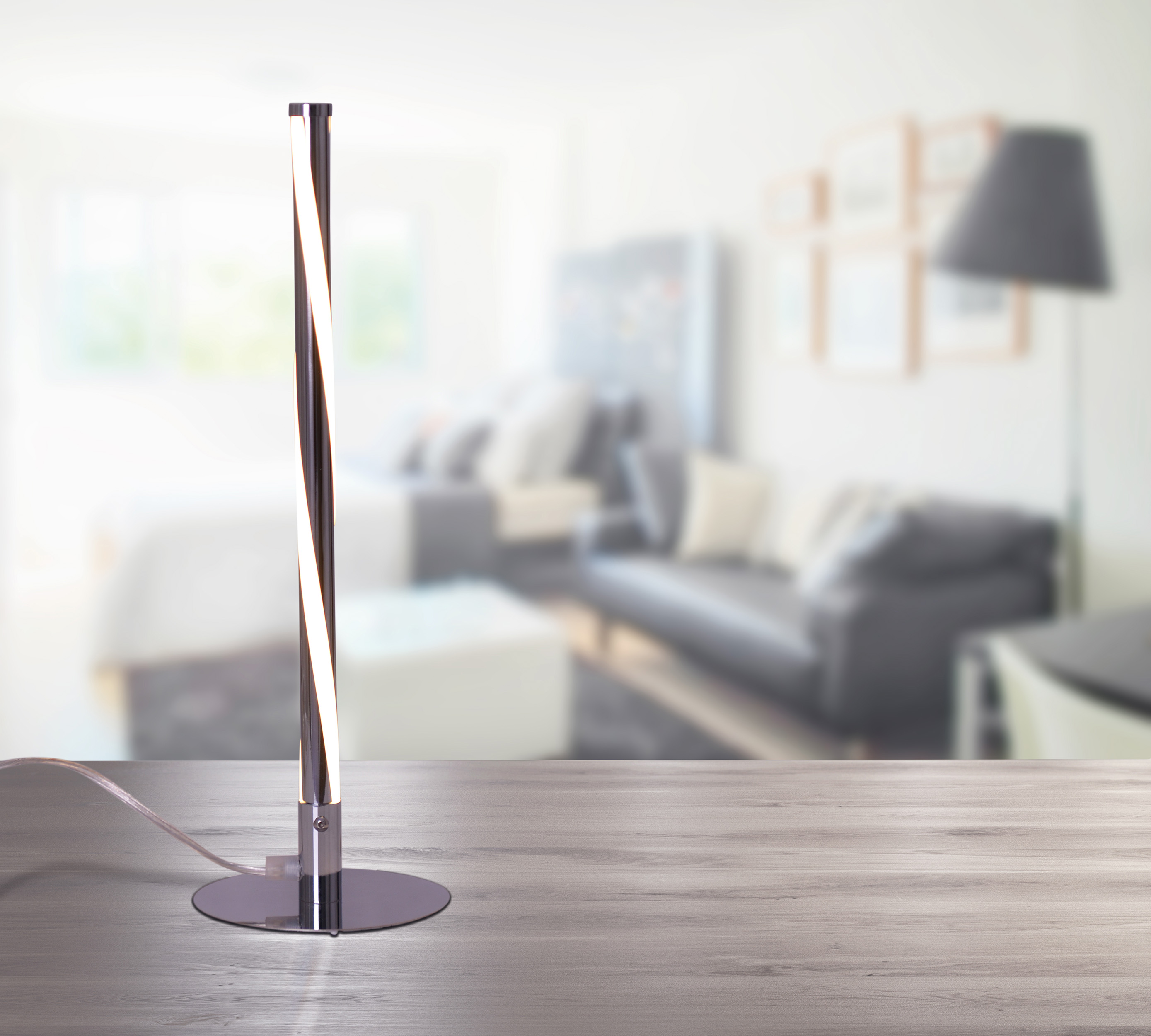 Eine silber-schwarze moderne Lampe mit Spiraldesign auf einem Holztisch.