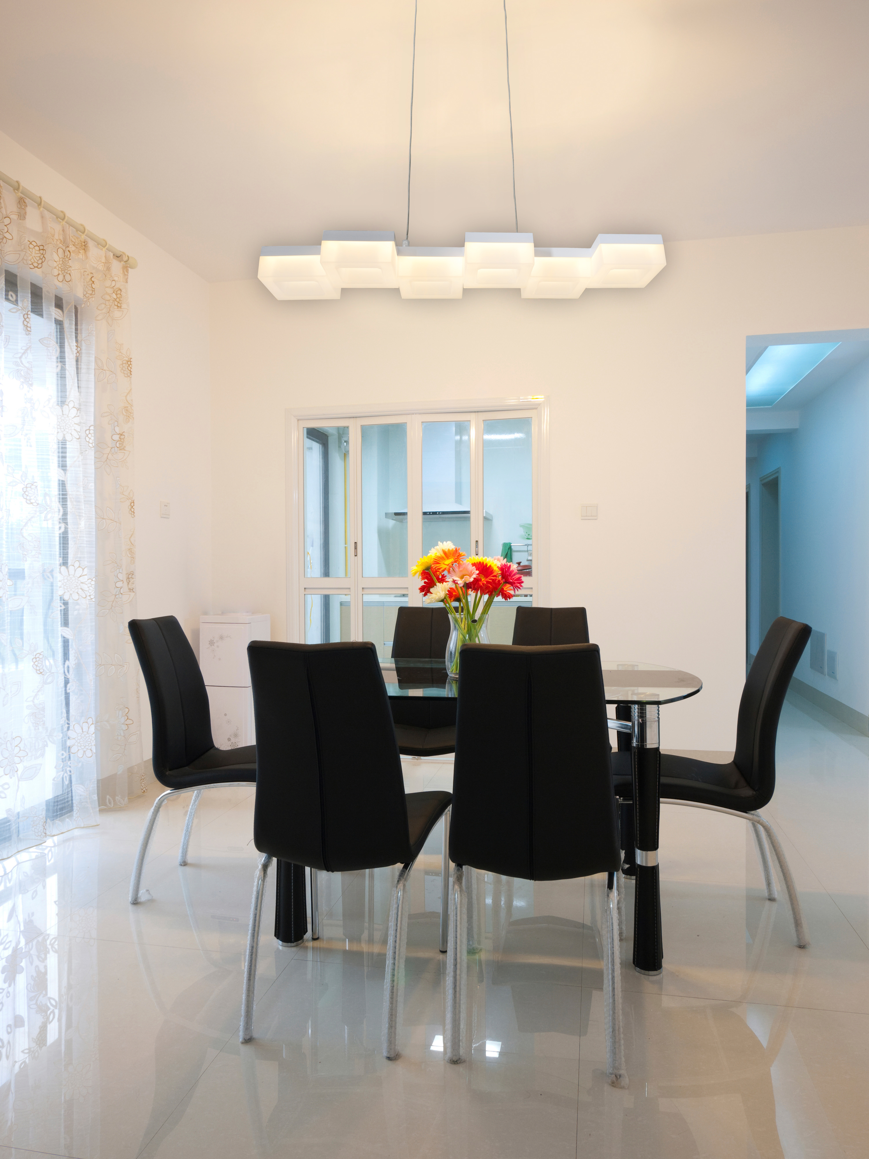 Esszimmer mit Glastisch, schwarzen Stühlen und moderner Leuchte über einer Blumenvase.