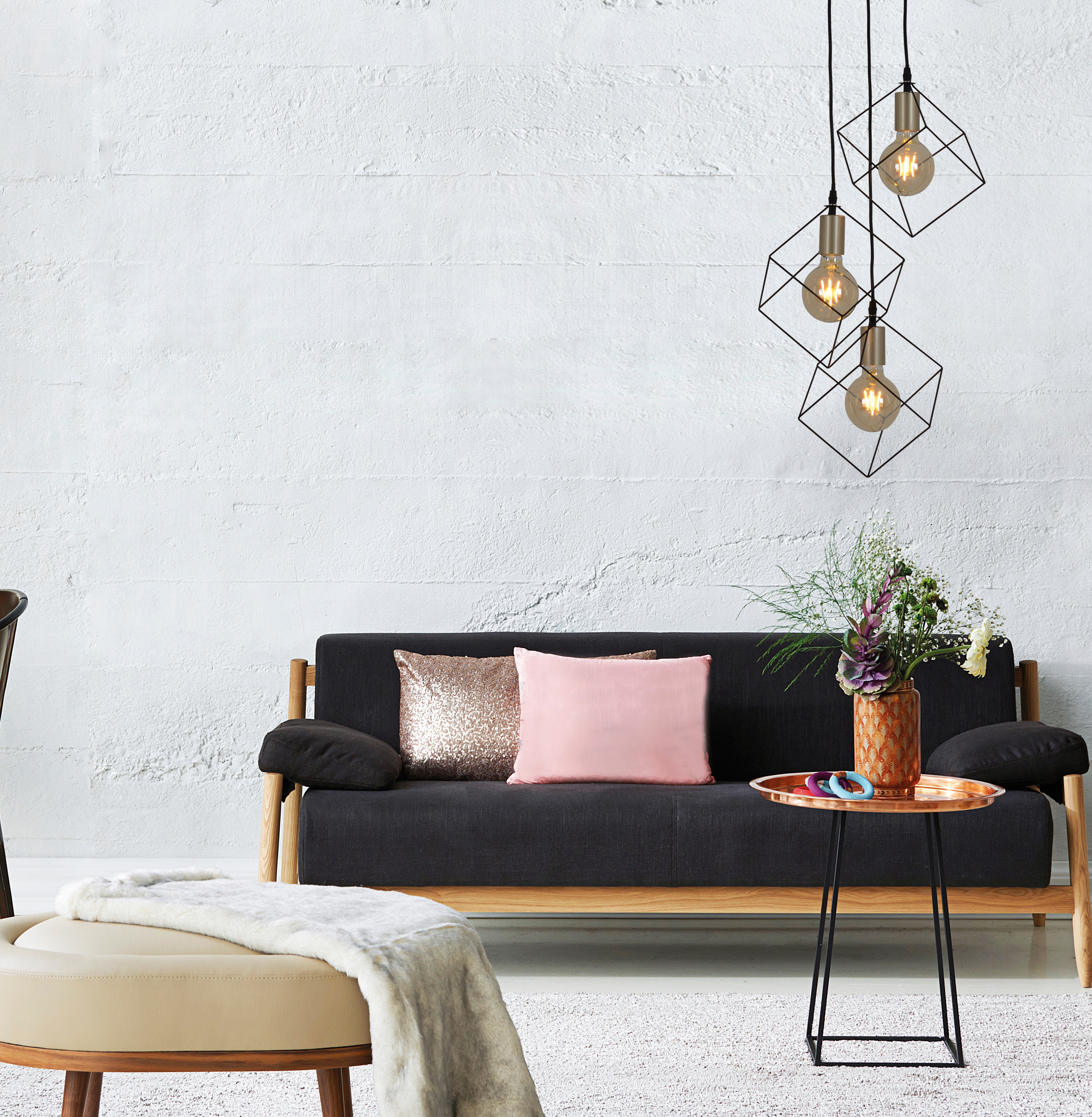 Wohnzimmerszene mit Sofa, Kissen, Tisch mit Deko und geometrischen Hängelampen.