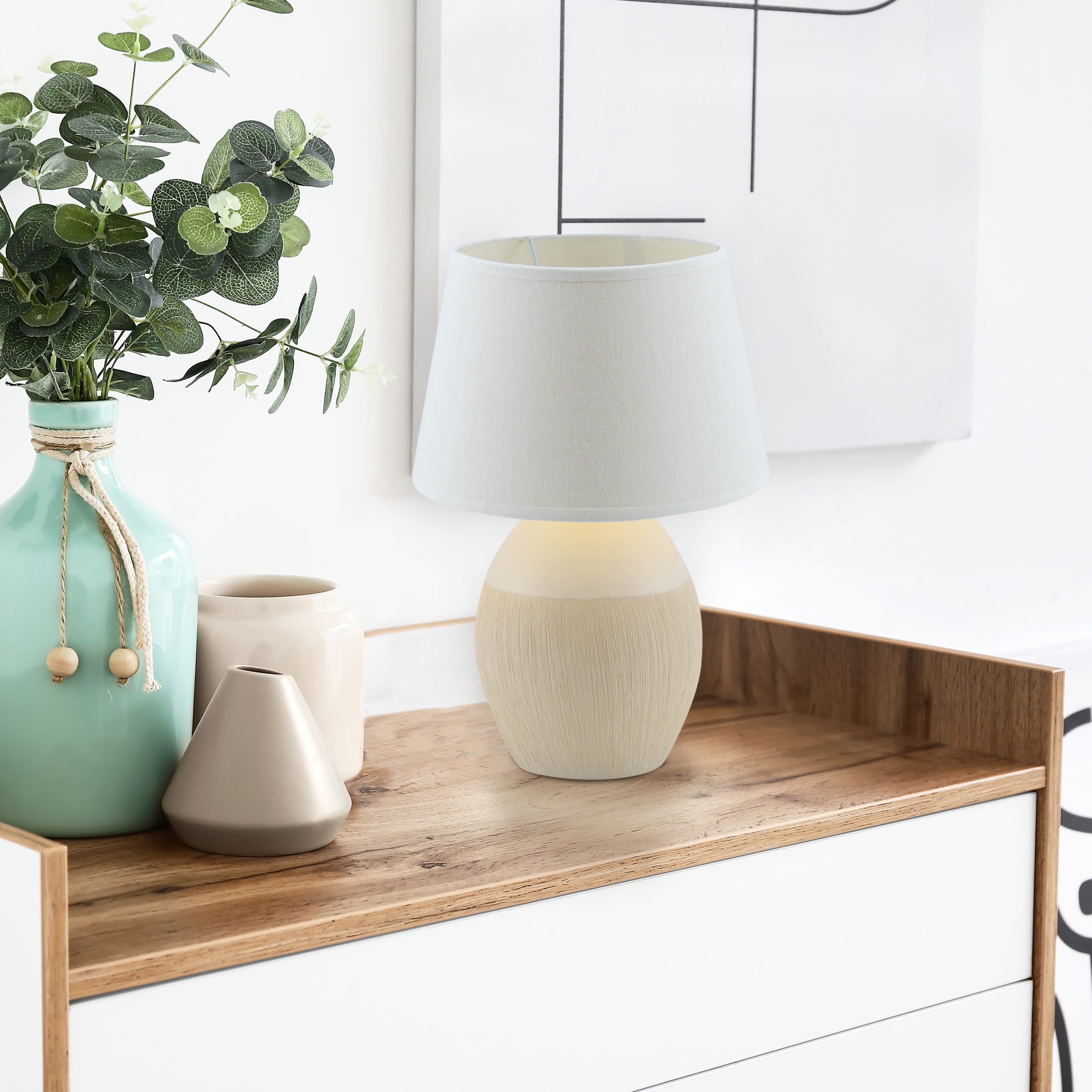 Eine Tischlampe auf einer Holzoberfläche, mit Pflanzen und einer dekorativen Vase im Hintergrund.