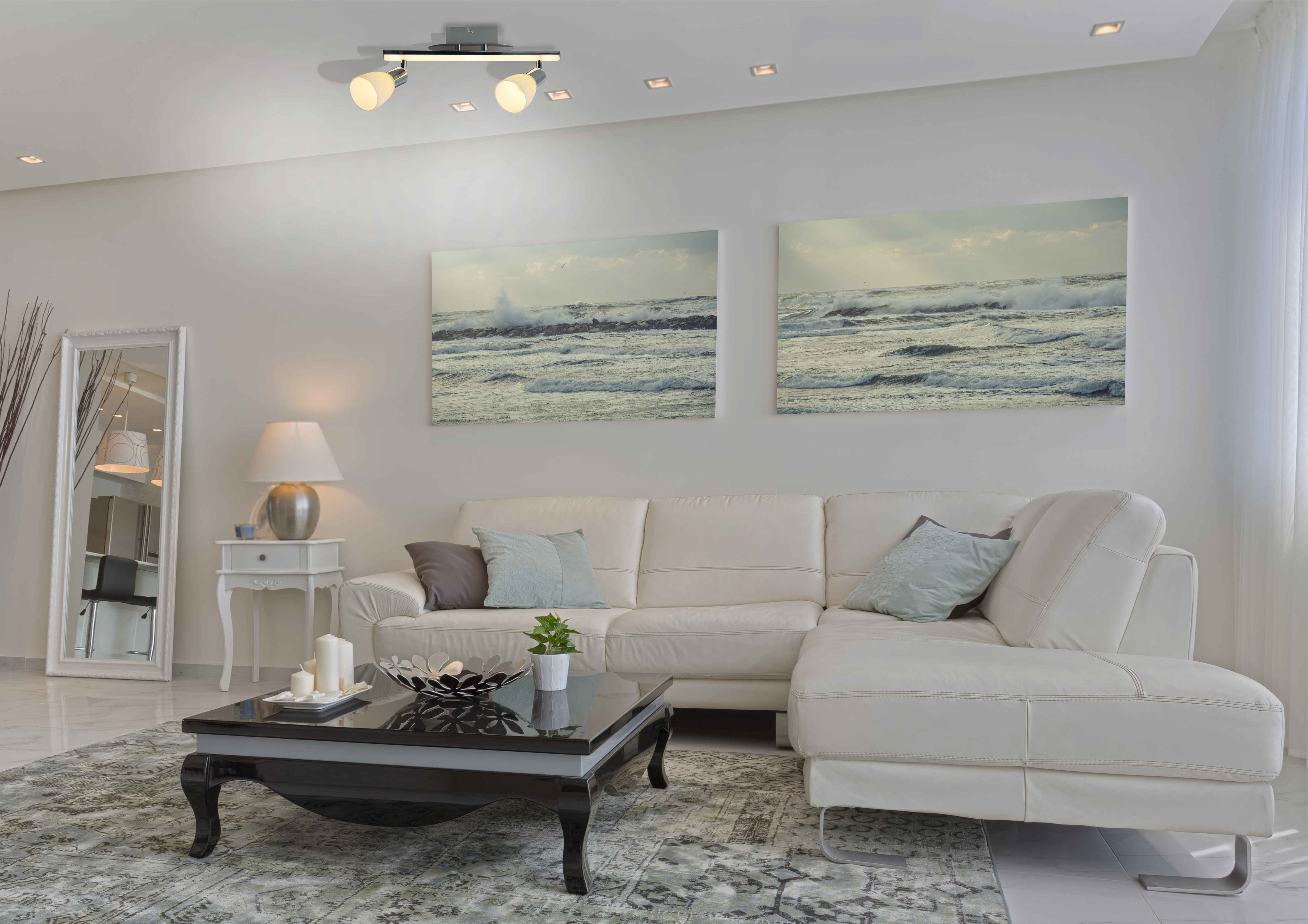 Wohnzimmer mit weißem Sofa, Couchtisch, Spiegel und Strandkunst.