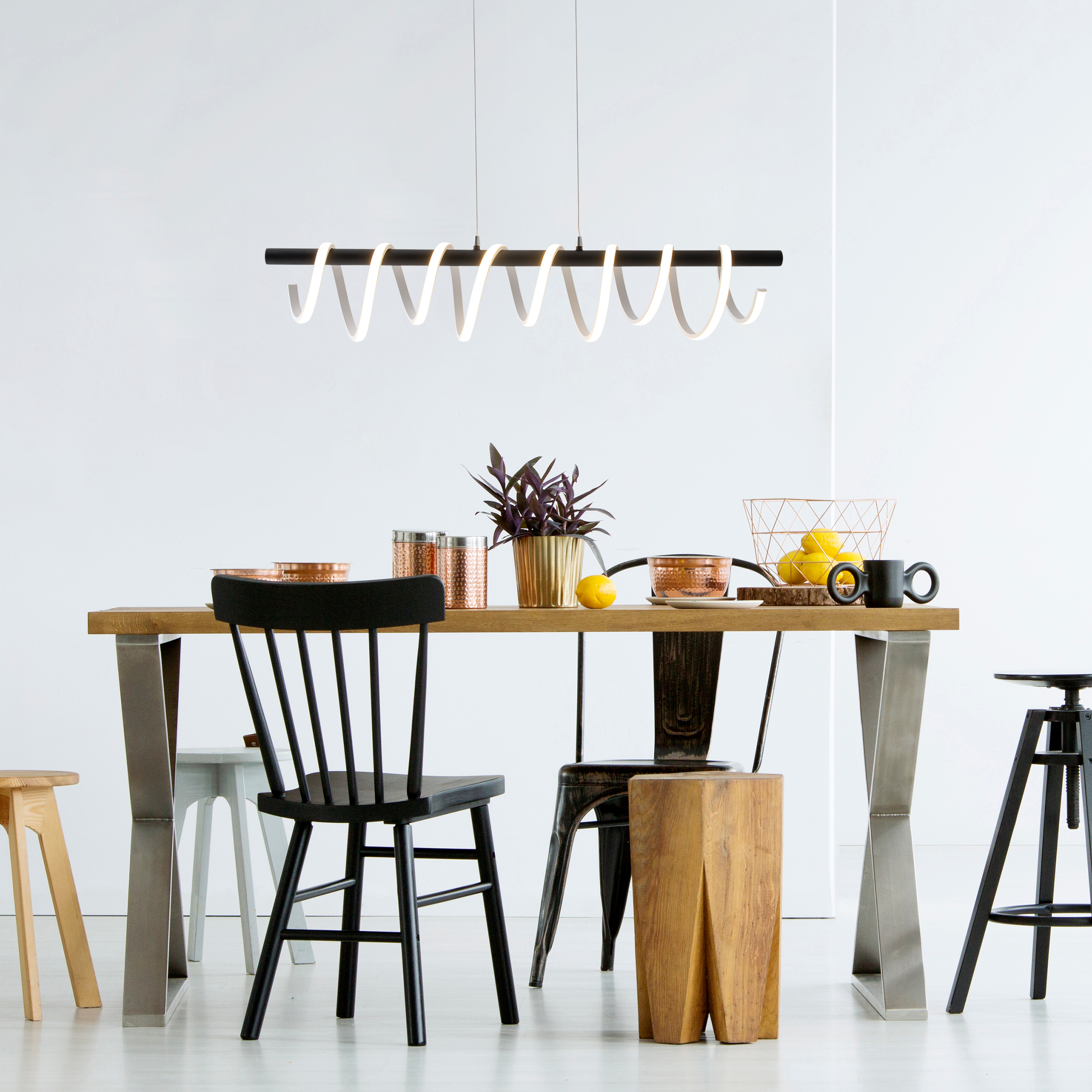 Esszimmer. Holztisch, schwarzer Stuhl, Kupferkessel, gelbe Zitronen und eine moderne Hängeleuchte.