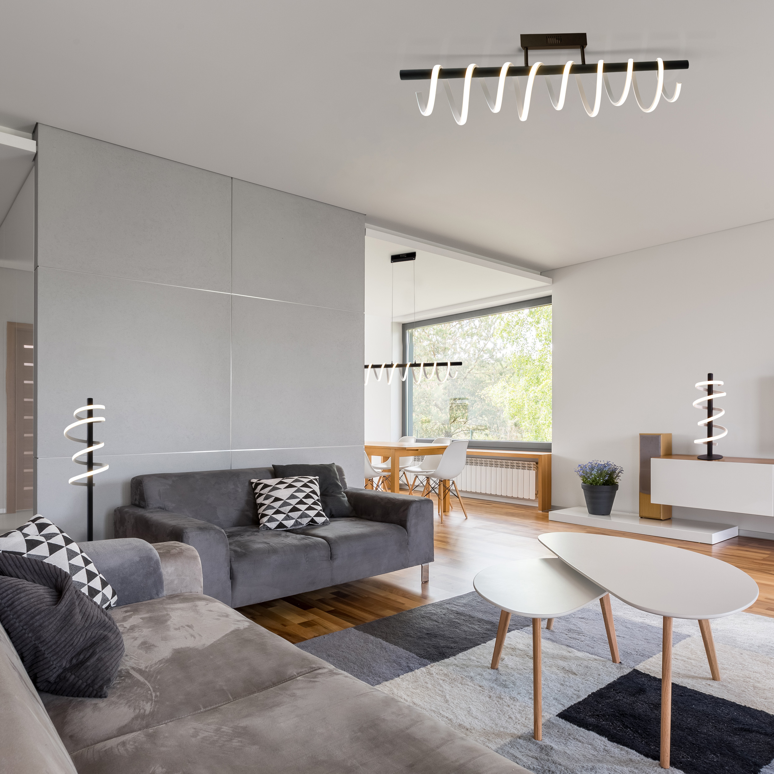 Modernes Wohnzimmer mit grauem Sofa, weißen Tischen und einer spiralförmigen Stehlampe.