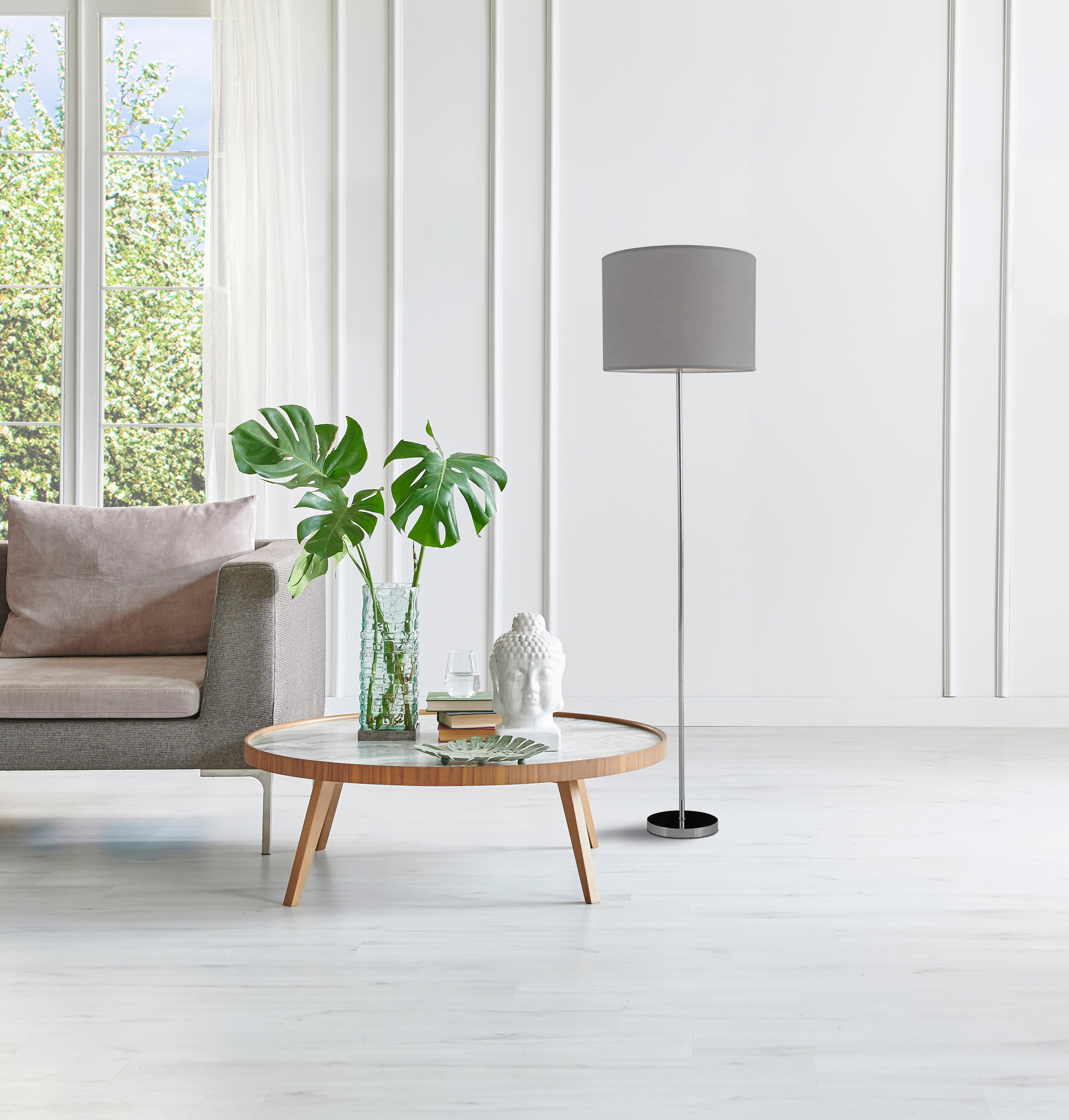 Ein Wohnzimmer mit einem grauen Sofa, einem Tisch mit Vase und einer Lampe.