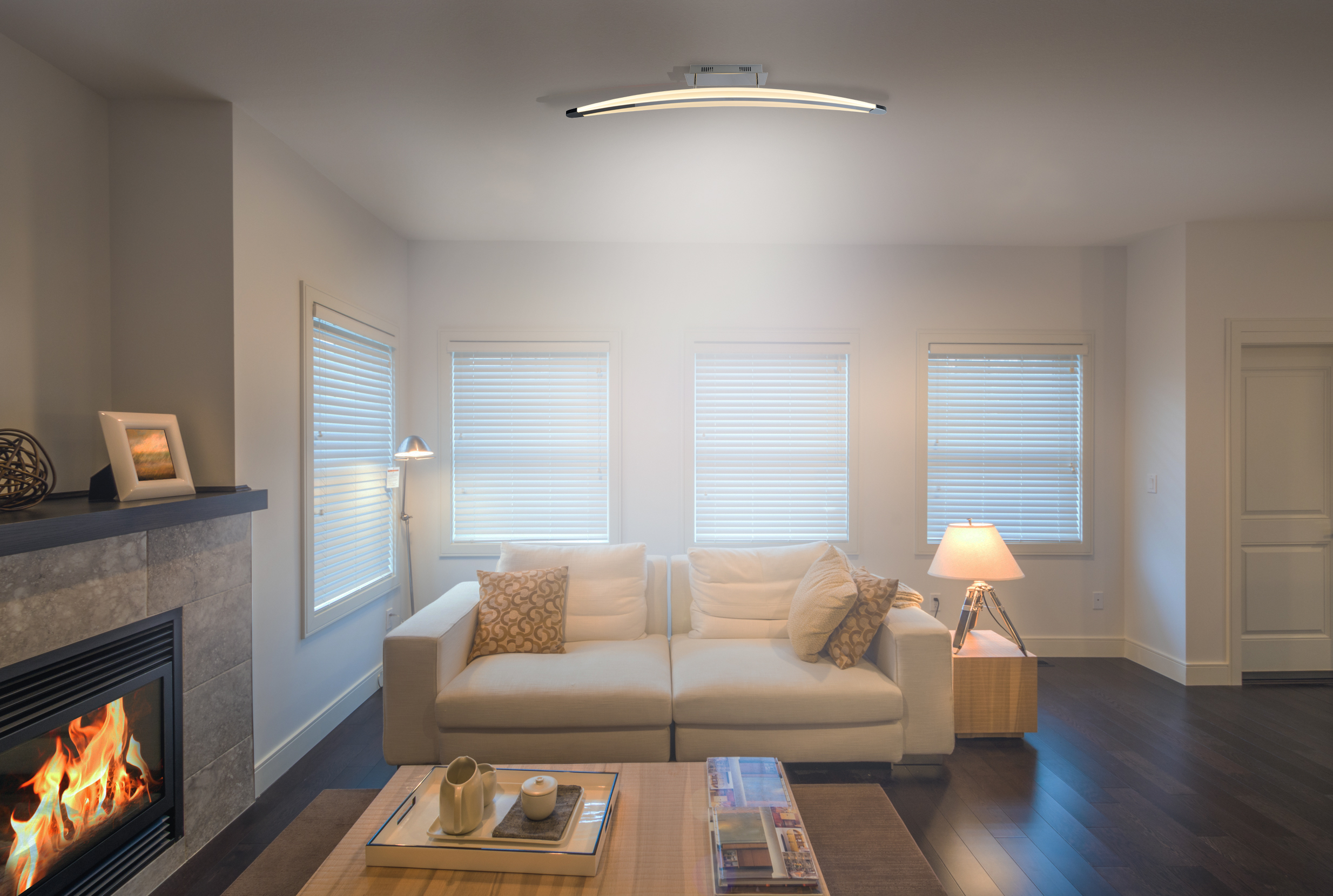 Wohnzimmer mit Kamin, Sofa und Fenstern. Weiße Wände und Parkettboden.